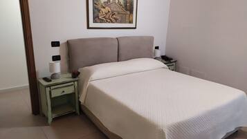 A neatly made bed with a white bedspread, a nightstand with a lamp, a remote control, and a small potted plant.