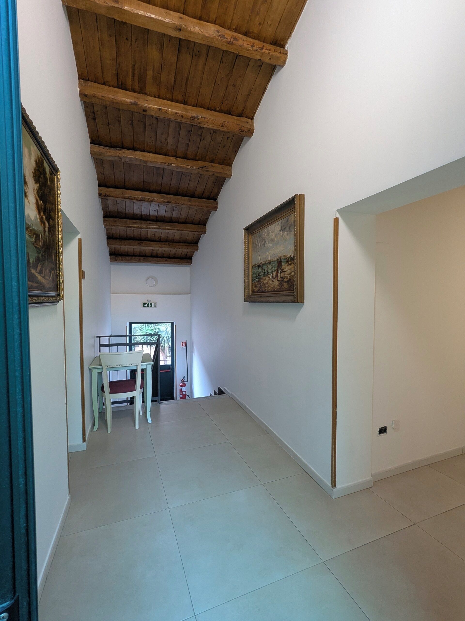 A hallway with a wooden ceiling, a dining area with a table and chairs, and a painting on the wall.