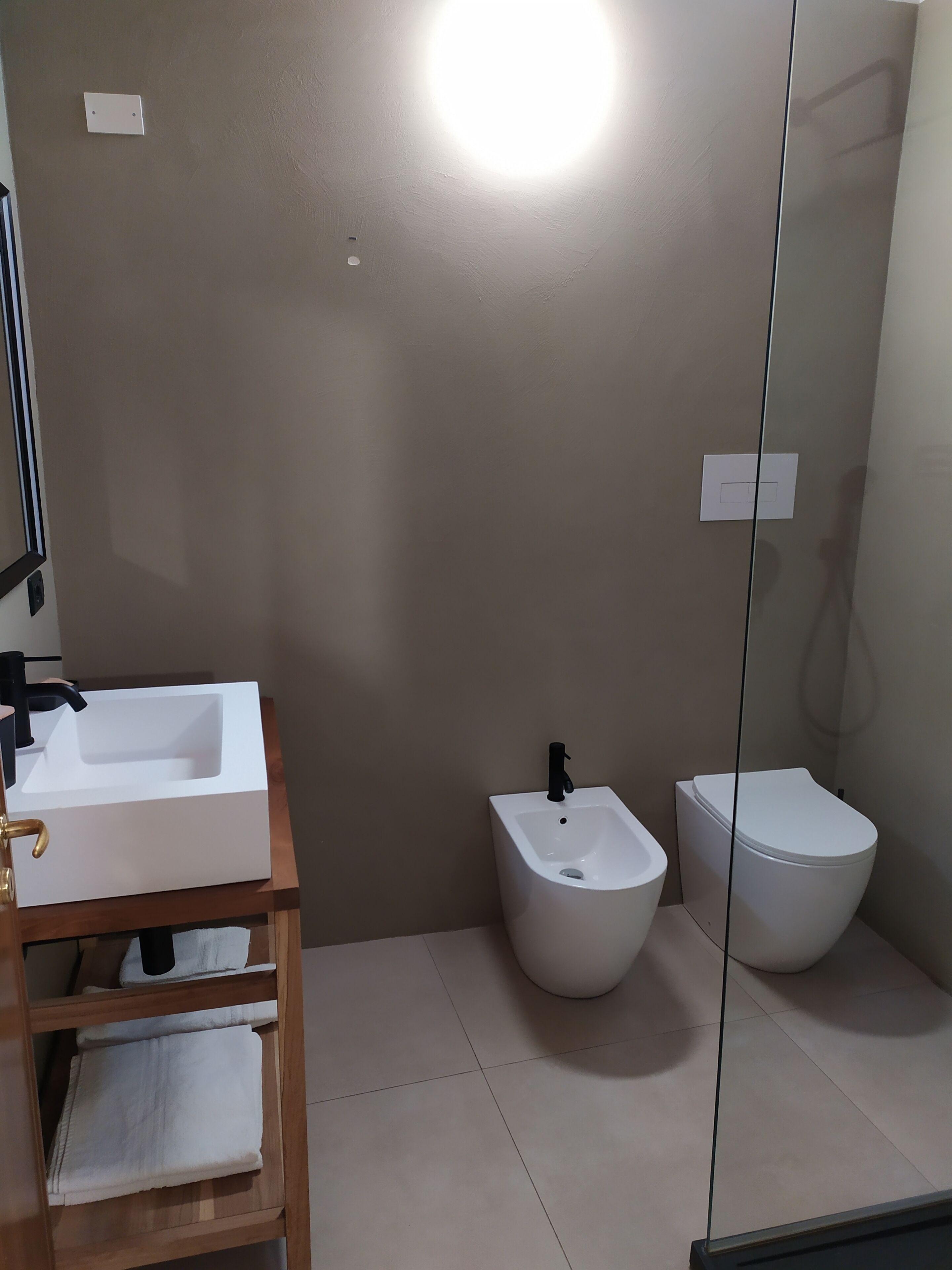 Un baño con lavamanos blanco, bidé y retrete, un perchero de madera y un espejo.