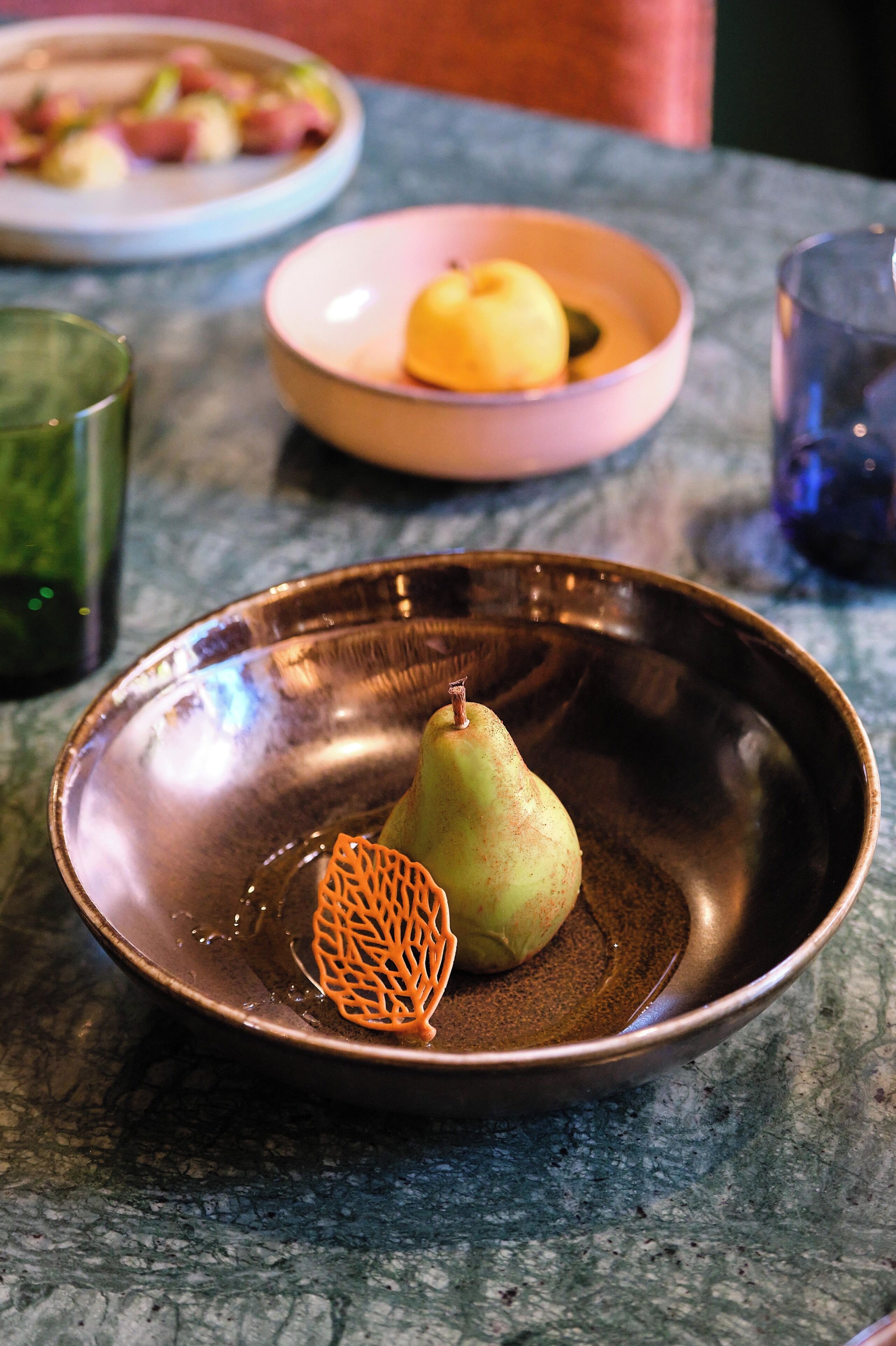 A table with a metal bowl containing a pear and a decorative orange net.