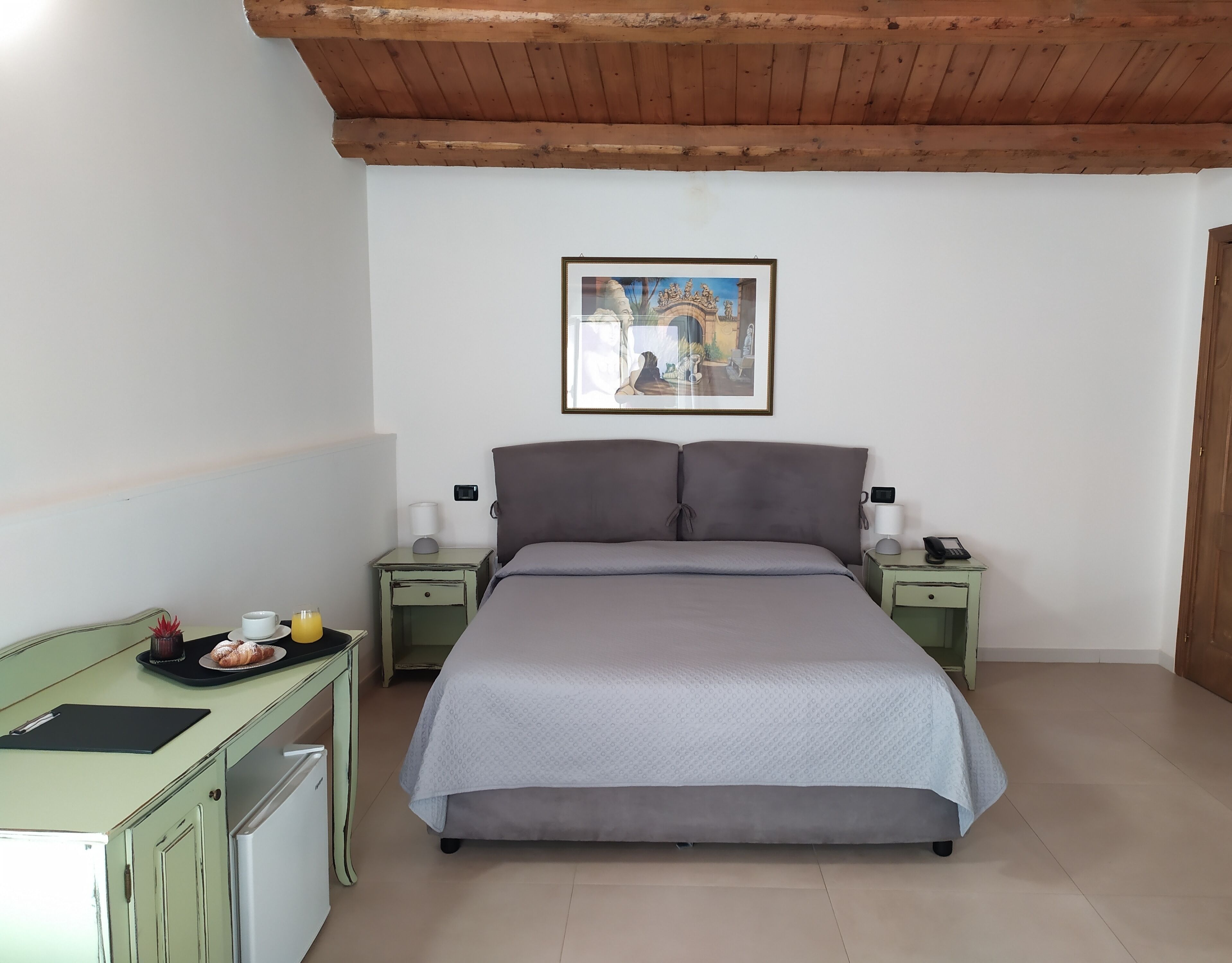 A bedroom with a bed, two bedside tables, a desk, a chair, and a framed picture on the wall.
