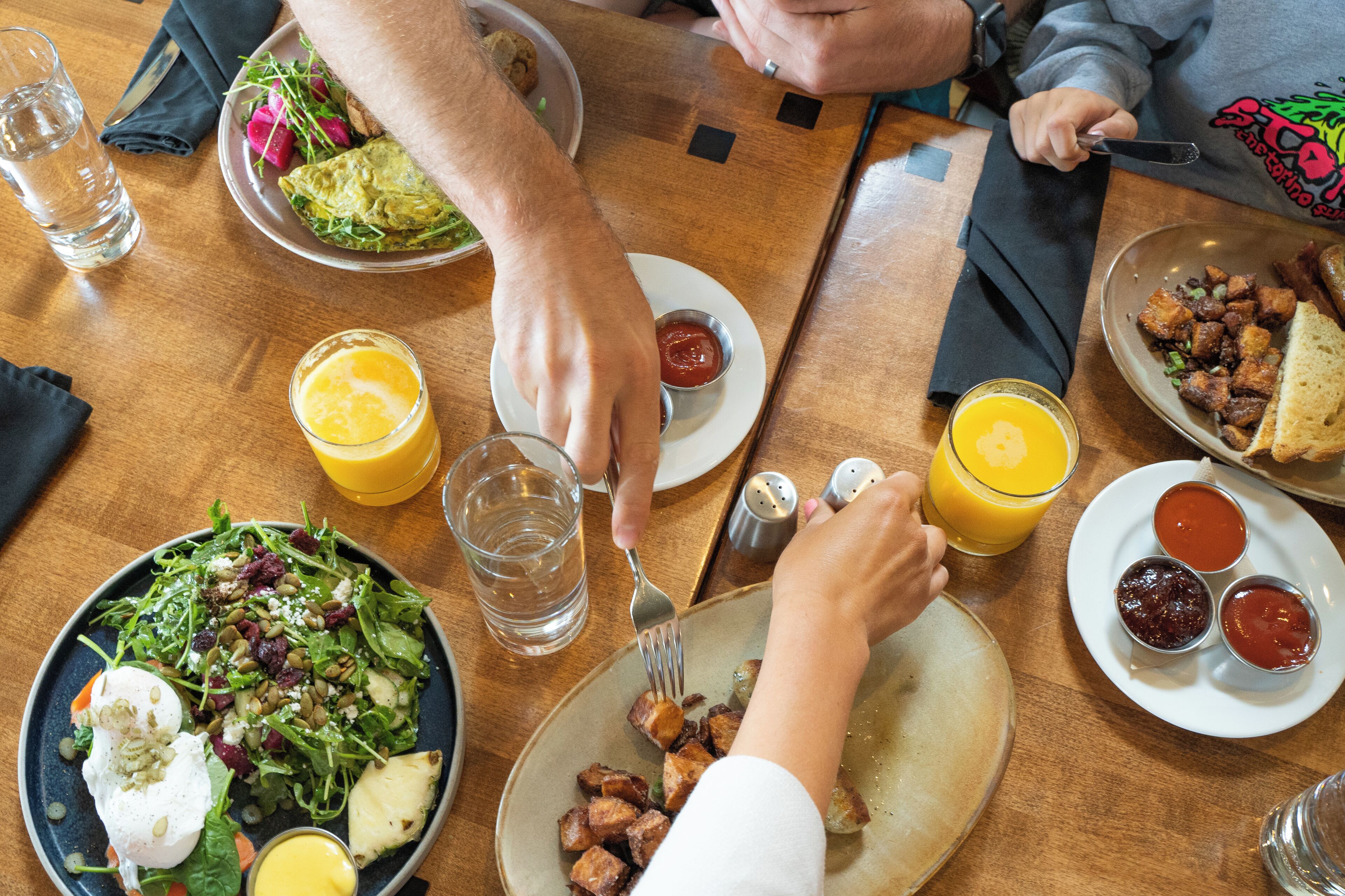 A dining table with plates of food, glasses of orange juice, and a salt and pepper shaker.
