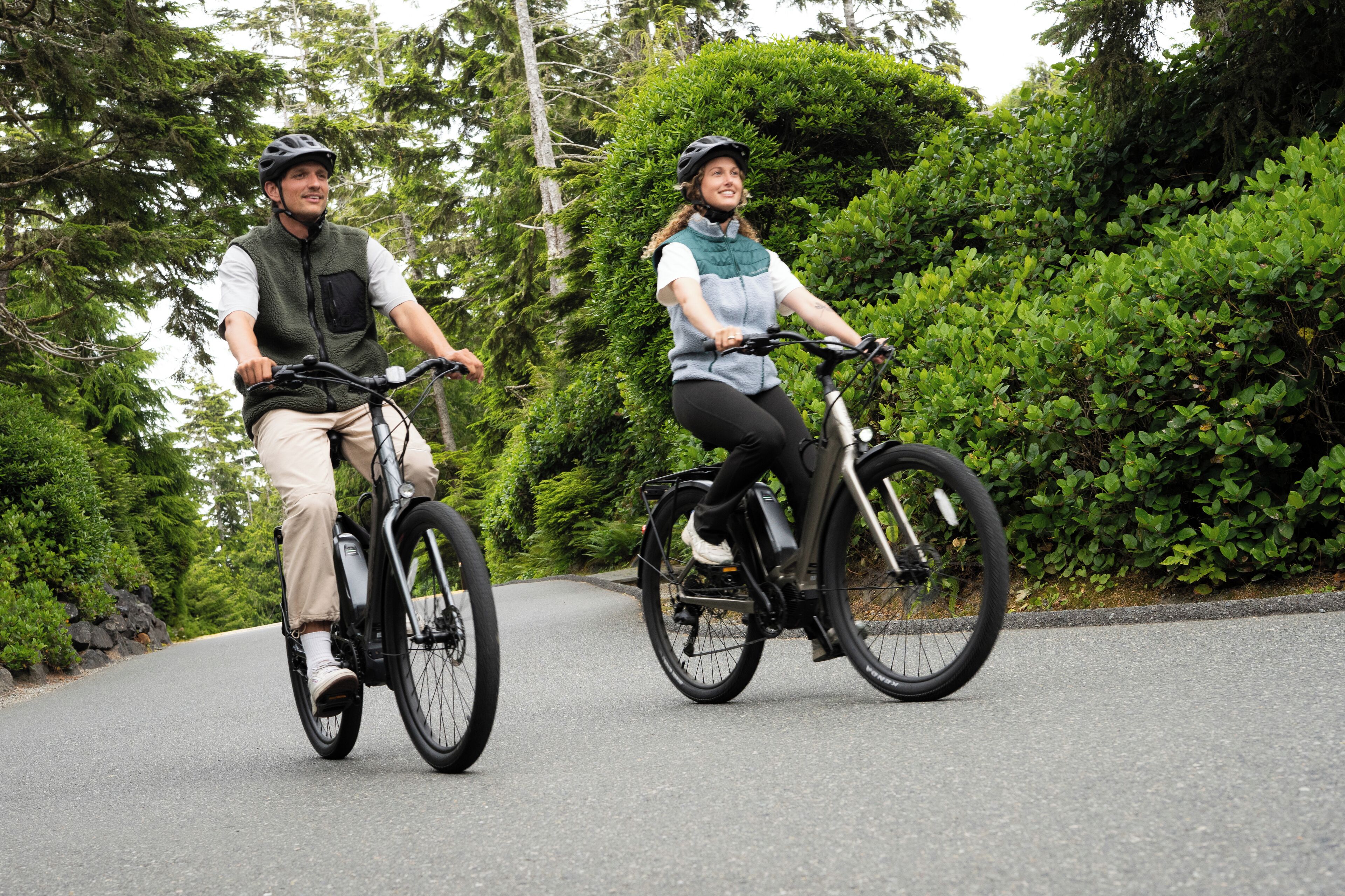 Two people riding bicycles on a road surrounded by greenery.