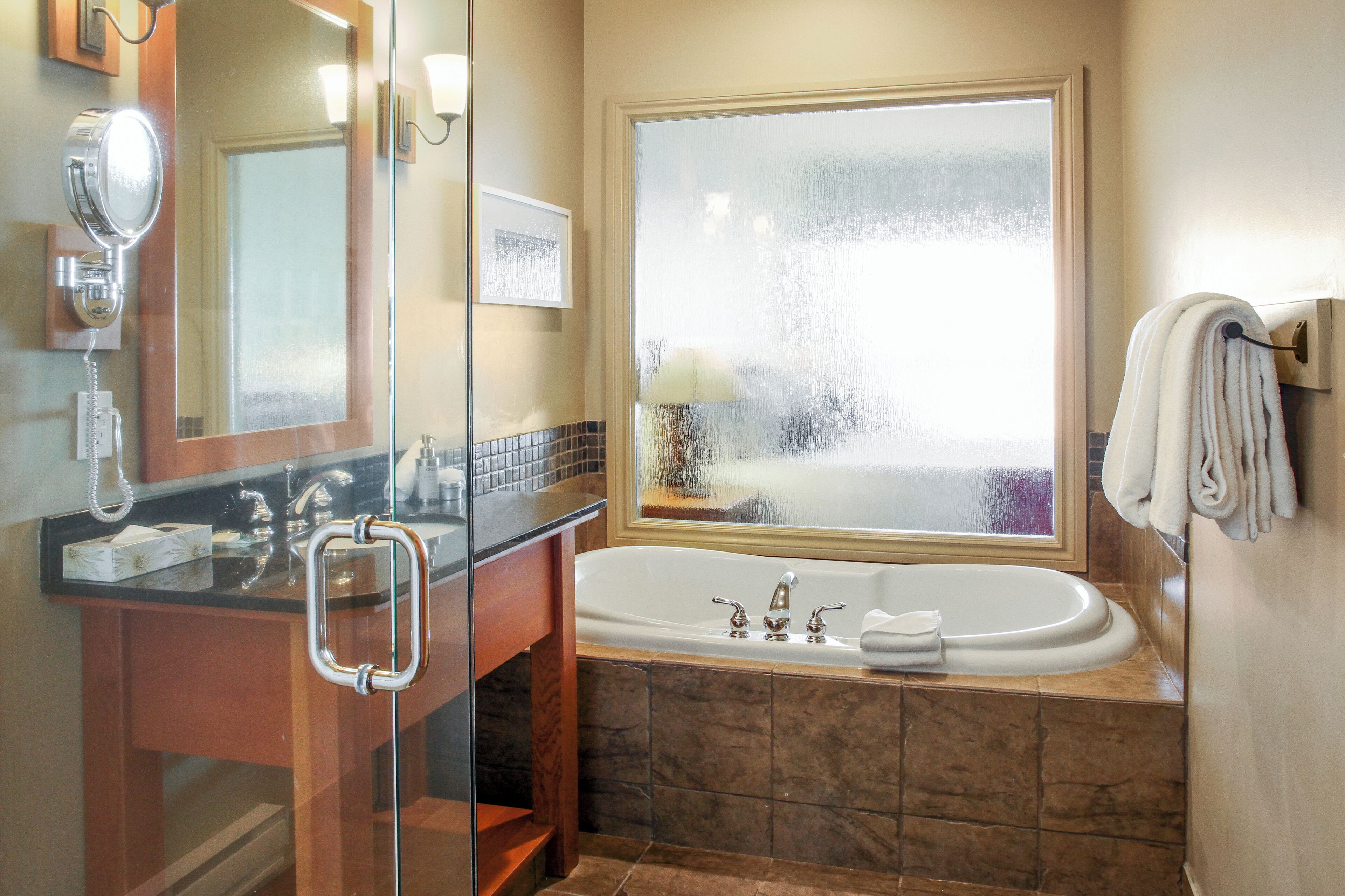 Une salle de bain dotée d’une grande baignoire, d’une cabine de douche en verre, d’un meuble-lavabo avec miroir et d’une fenêtre à vitrage dépoli.