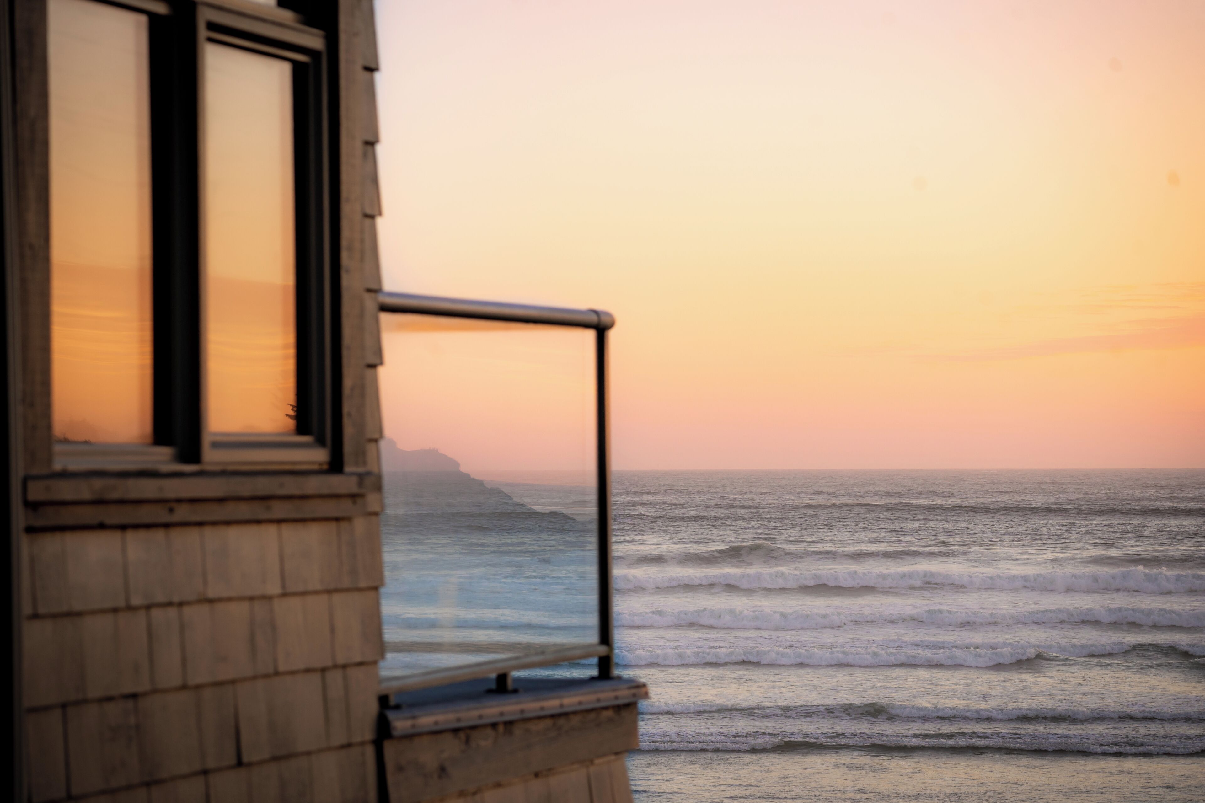 A wooden building with a balcony overlooking the ocean at sunset.