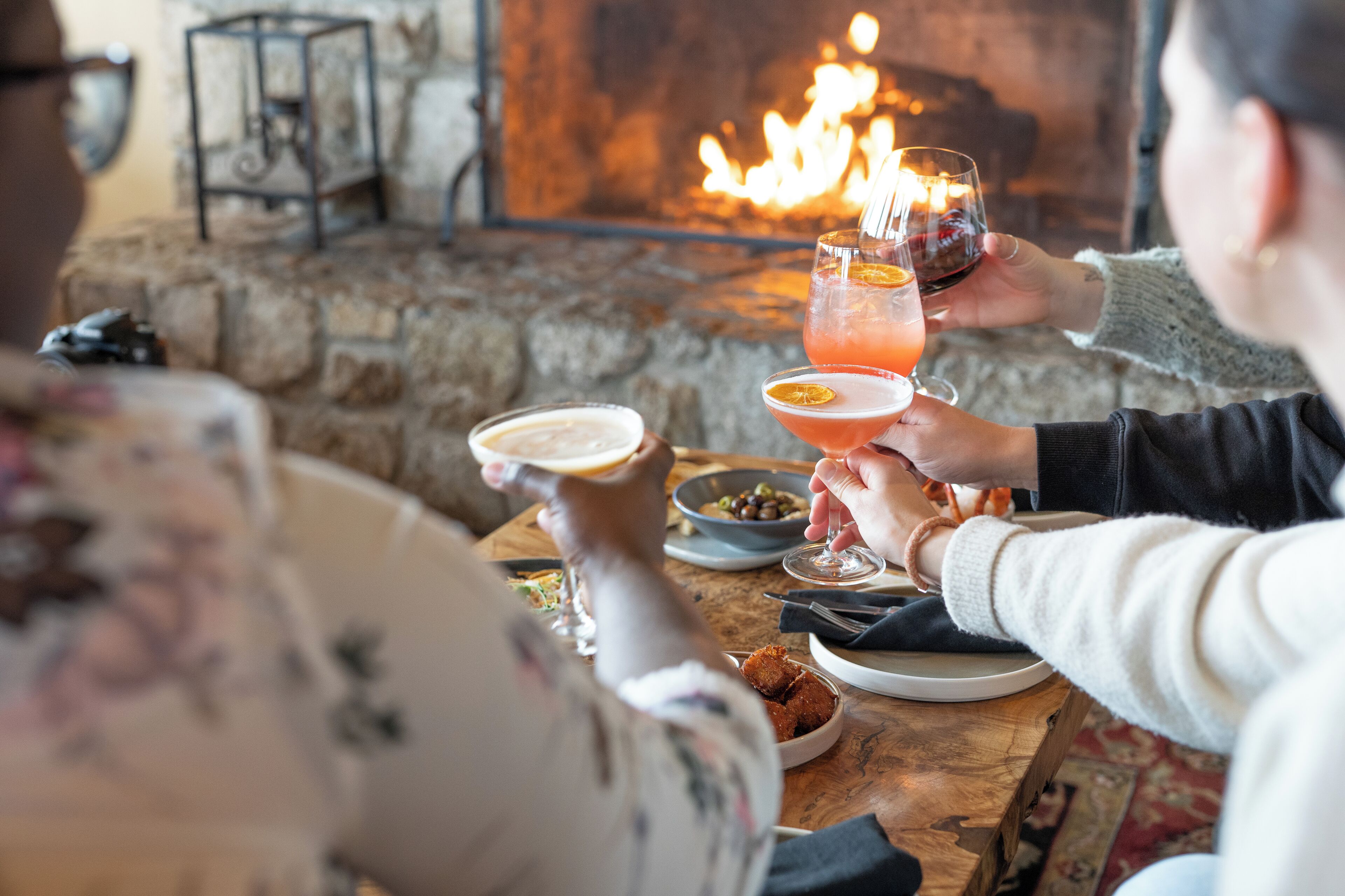 A cozy dining area with a stone fireplace, wooden table, and various dishes and drinks.