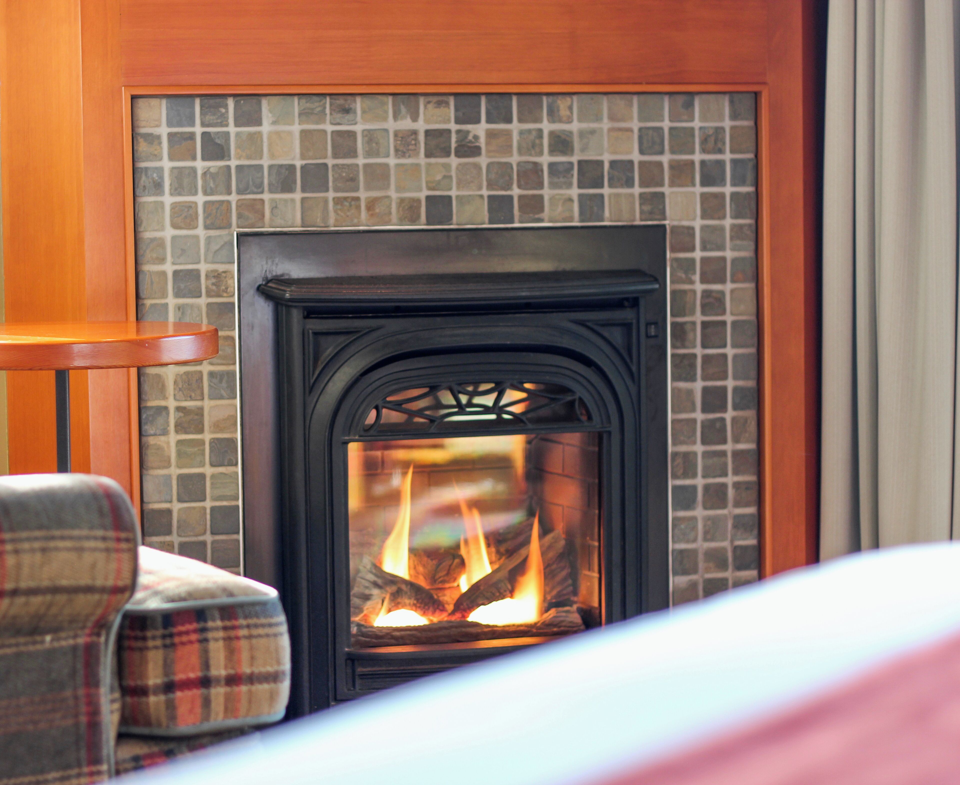 Una chimenea con detalles de azulejos, un sillón a cuadros y una mesa de madera.