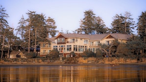 A large, multi-story house with a prominent balcony, situated by a lake with dense trees in the background. - Long Beach Lodge Resort (Tofino)