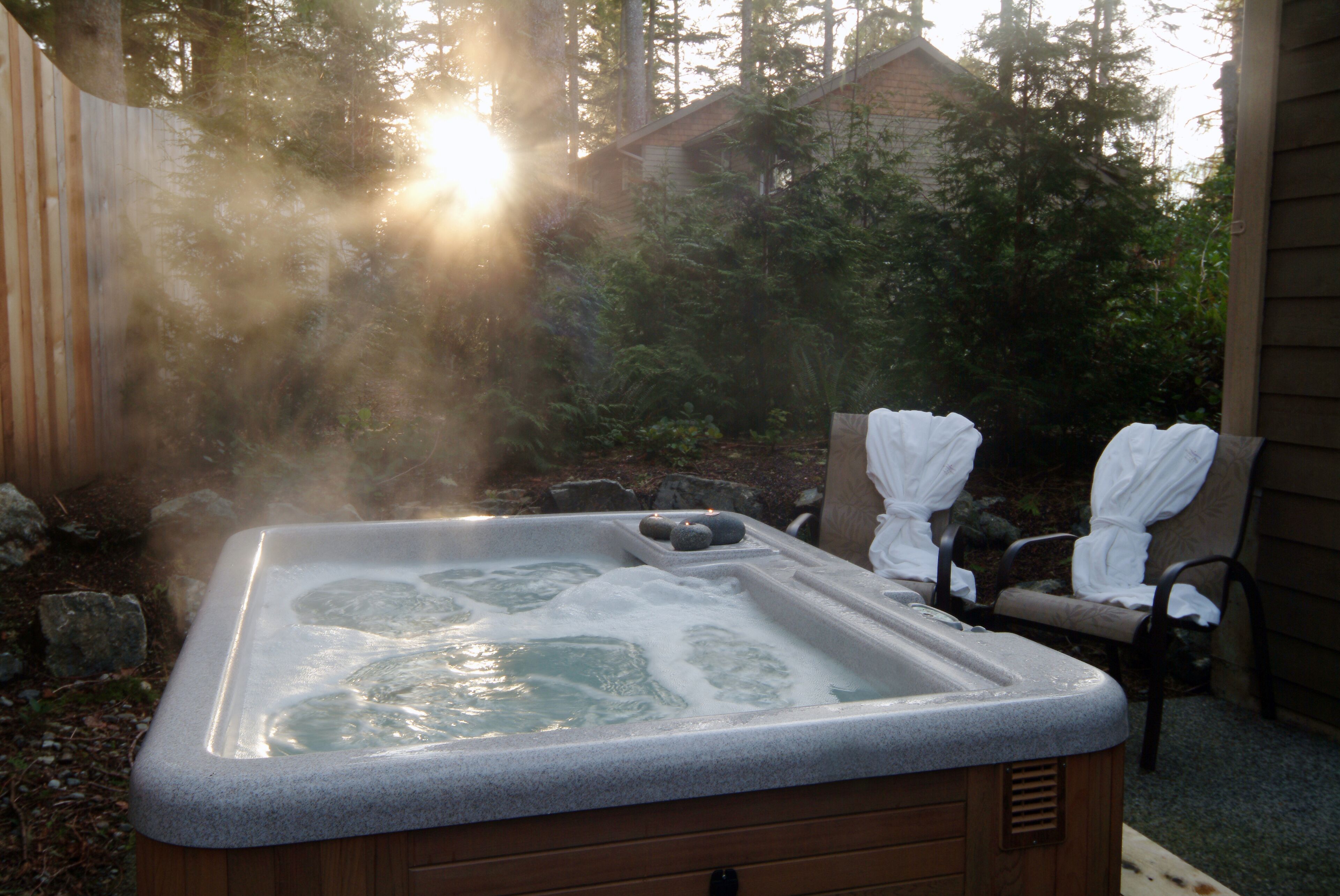 Een hottub met een houten buitenkant, omgeven door een houten omheining en bomen.