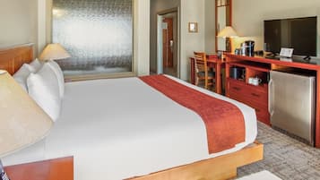 Ein Hotelzimmer mit einem großen Bett, einem Schreibtisch mit Fernseher, einem Kühlschrank und einem Fenster mit Milchglasverglasung.