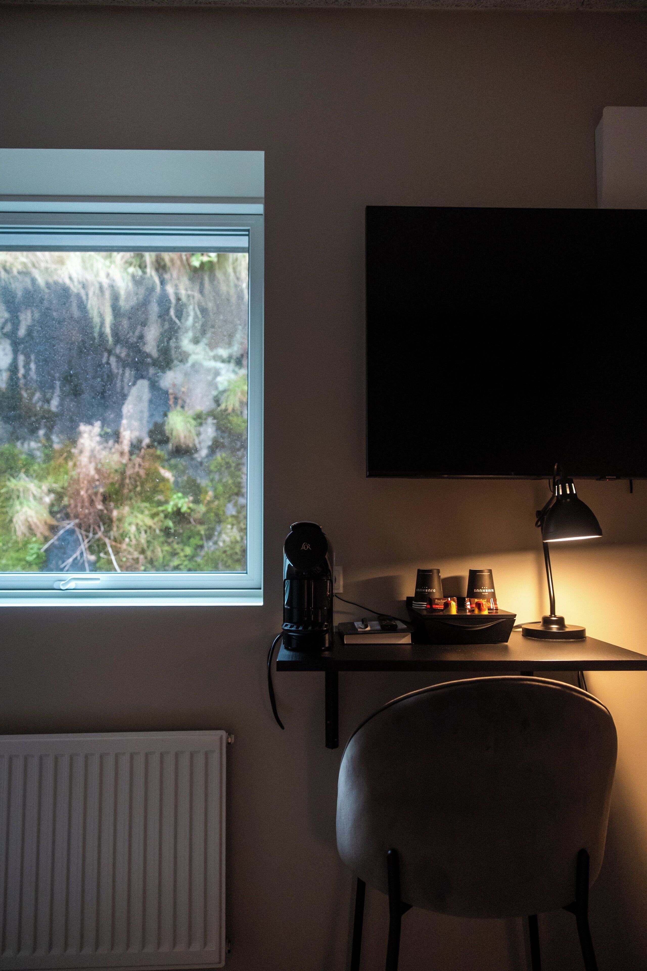 A room with a window, a desk with a lamp, a chair, and a radiator.