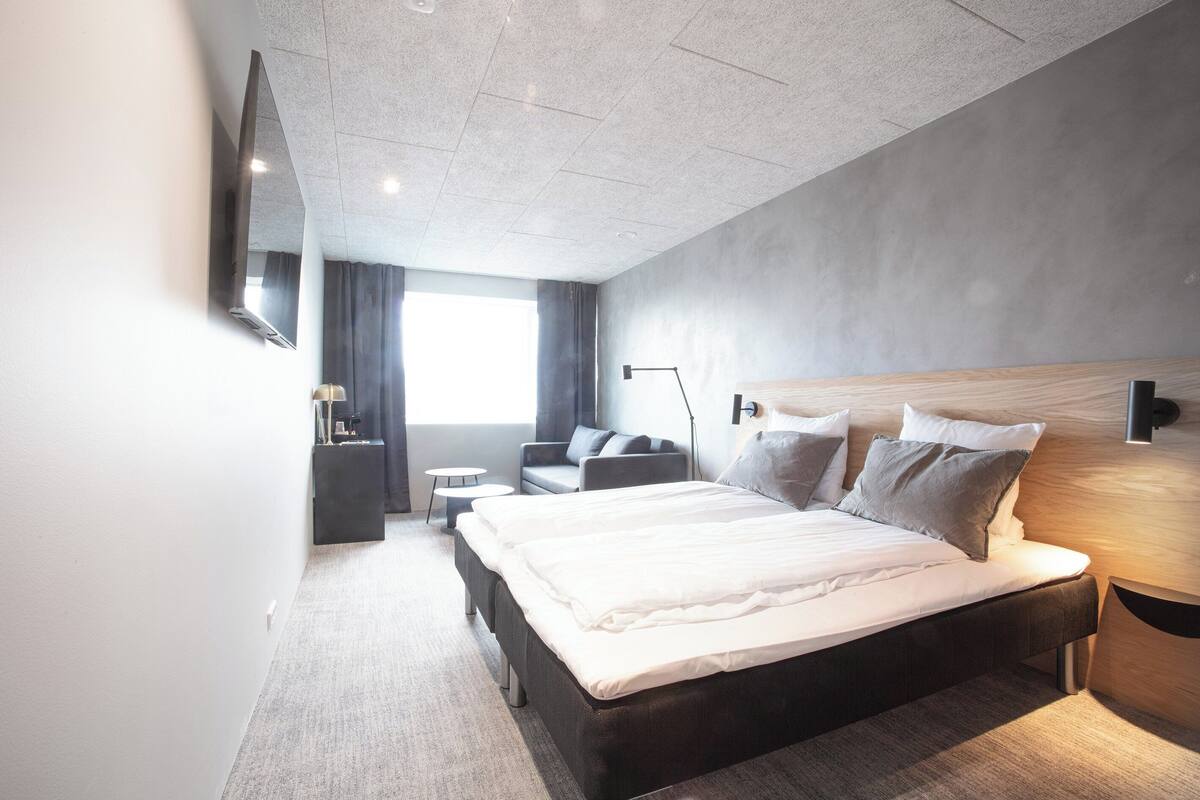 Une chambre d’hôtel moderne équipée d’un grand lit, d’un bureau, d’une chaise et d’un téléviseur à écran plat fixé au mur.