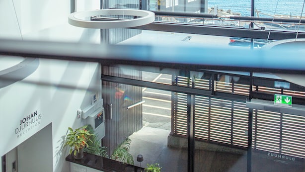 A modern reception area with a view of the sea and buildings across the water. - Hotel Djurhuus (Tórshavn)