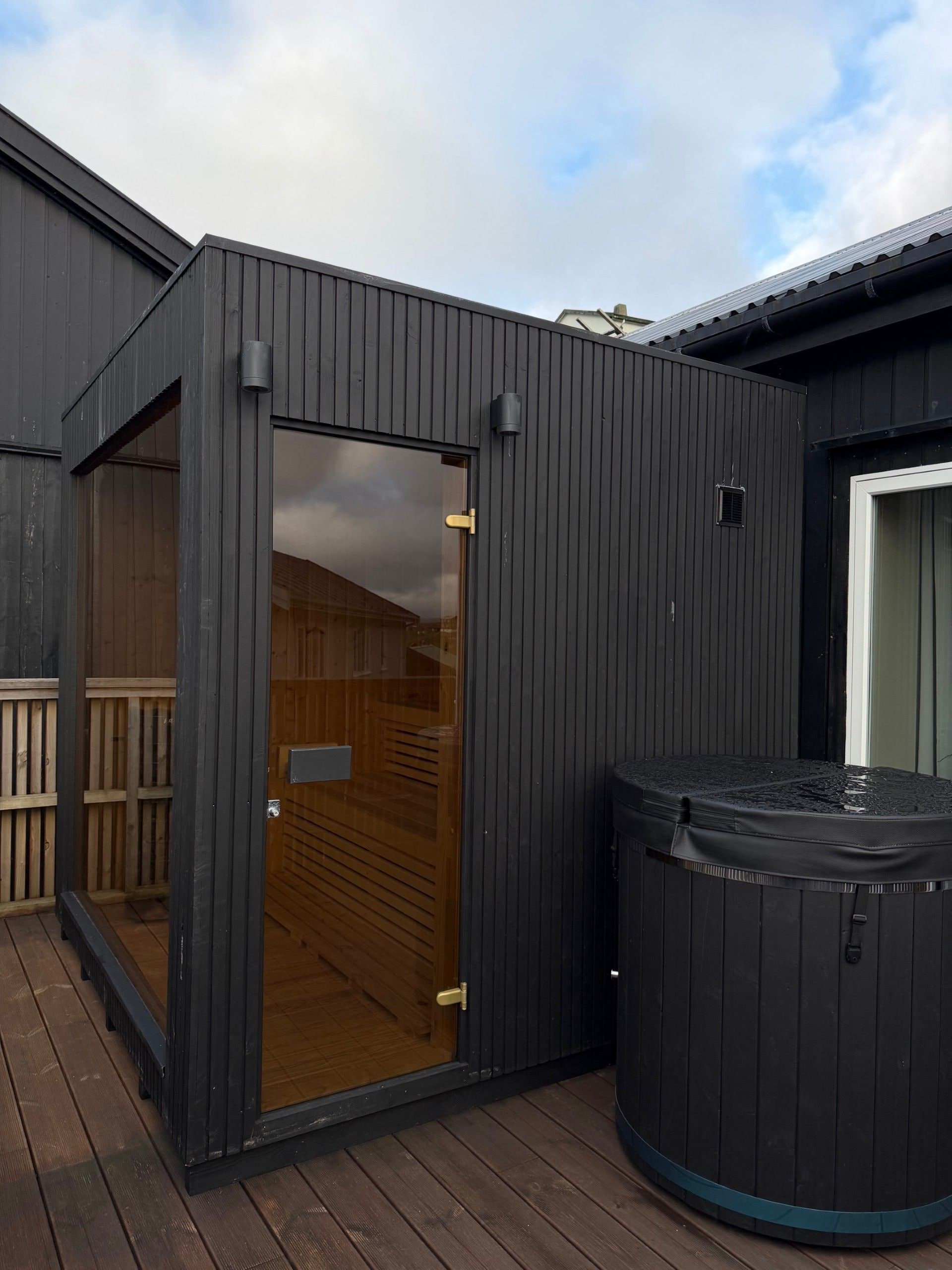 A wooden deck with a sauna and a glass door leading to a sauna room.