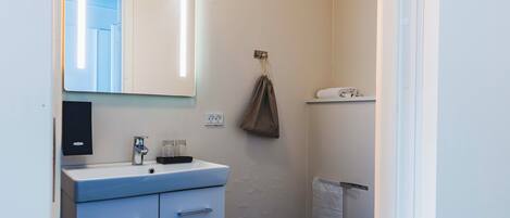 Un baño con lavamanos blanco, espejo y barra para toallas.