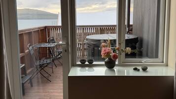 Una habitación con un ventanal grande que da a una terraza de madera y una masa de agua.