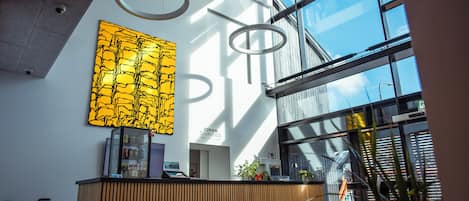 Een modern ingerichte receptie, met een receptiebalie, een groot abstract kunstwerk en een uitzicht op de lucht door grote ramen.