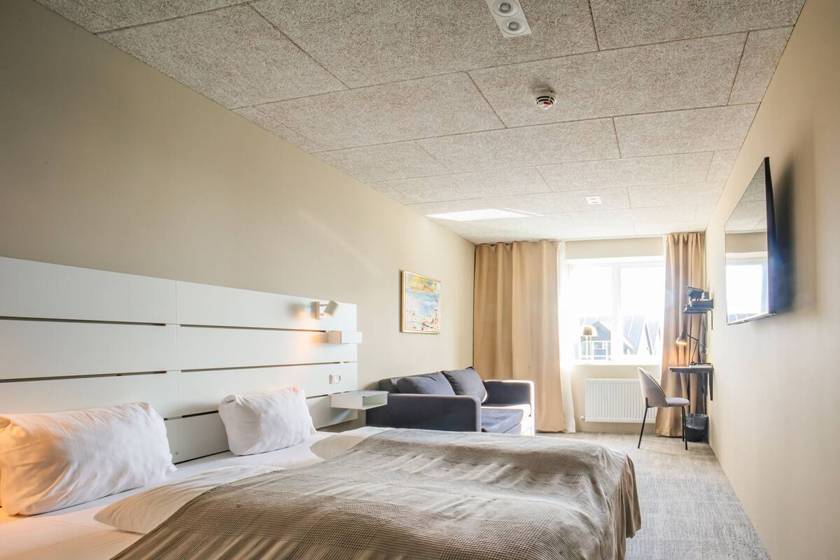 Une chambre d’hôtel avec un grand lit, un canapé, un bureau et une fenêtre avec des rideaux.
