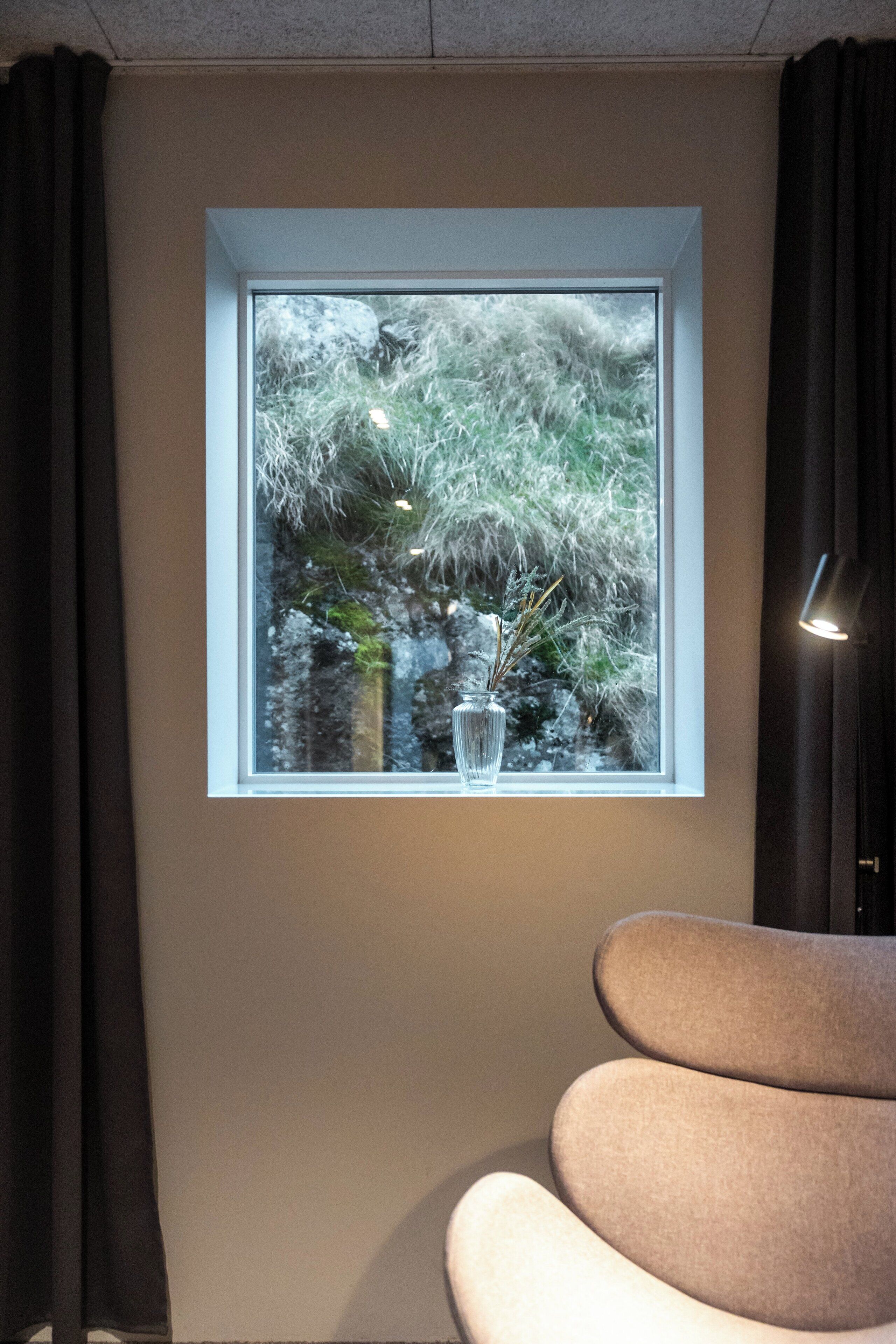Une pièce avec une fenêtre donnant sur un paysage enneigé, un vase contenant des plantes s échées et un fauteuil moderne.