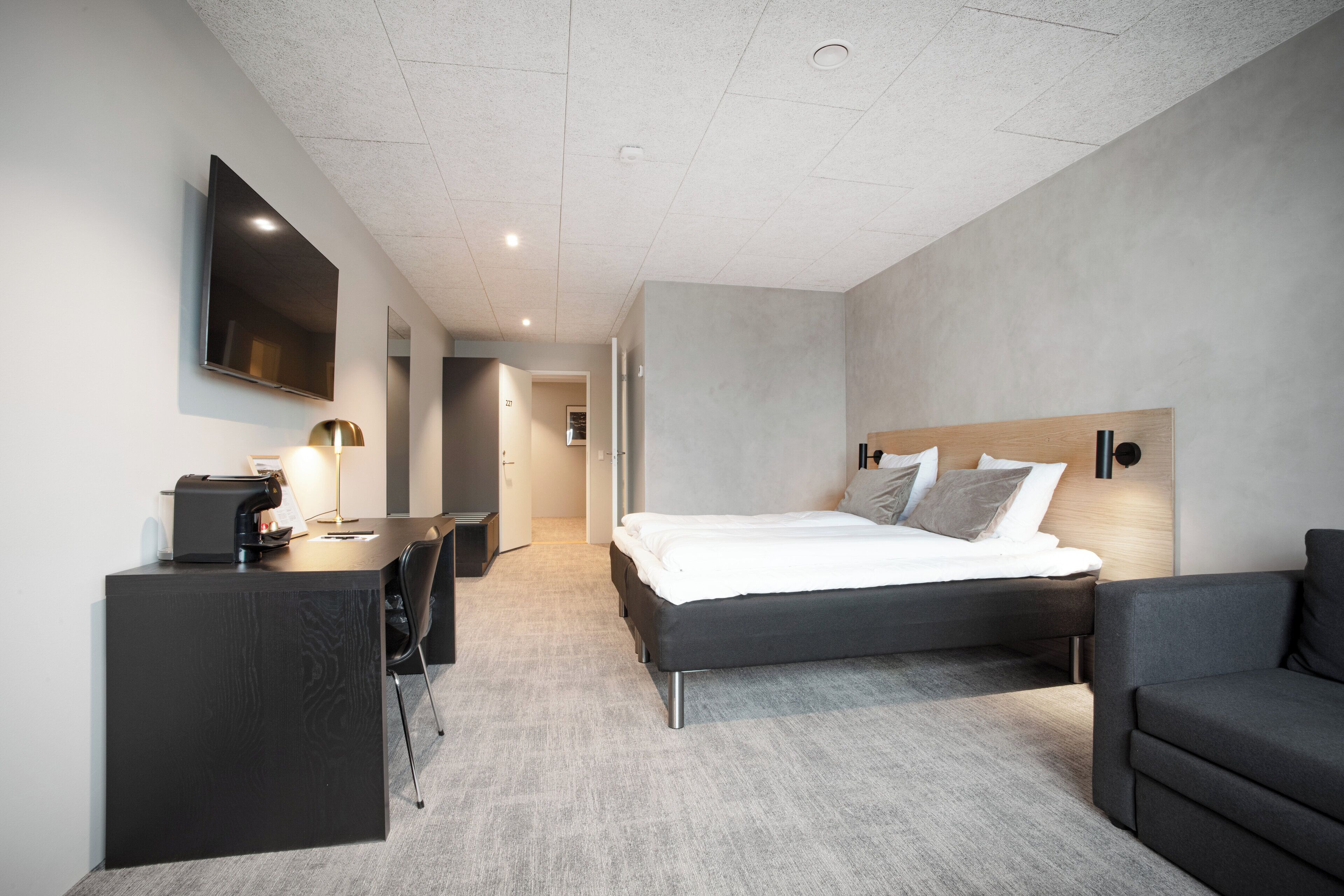 A modern hotel room with a bed, a desk, a chair, a flat-screen TV, and a sofa.