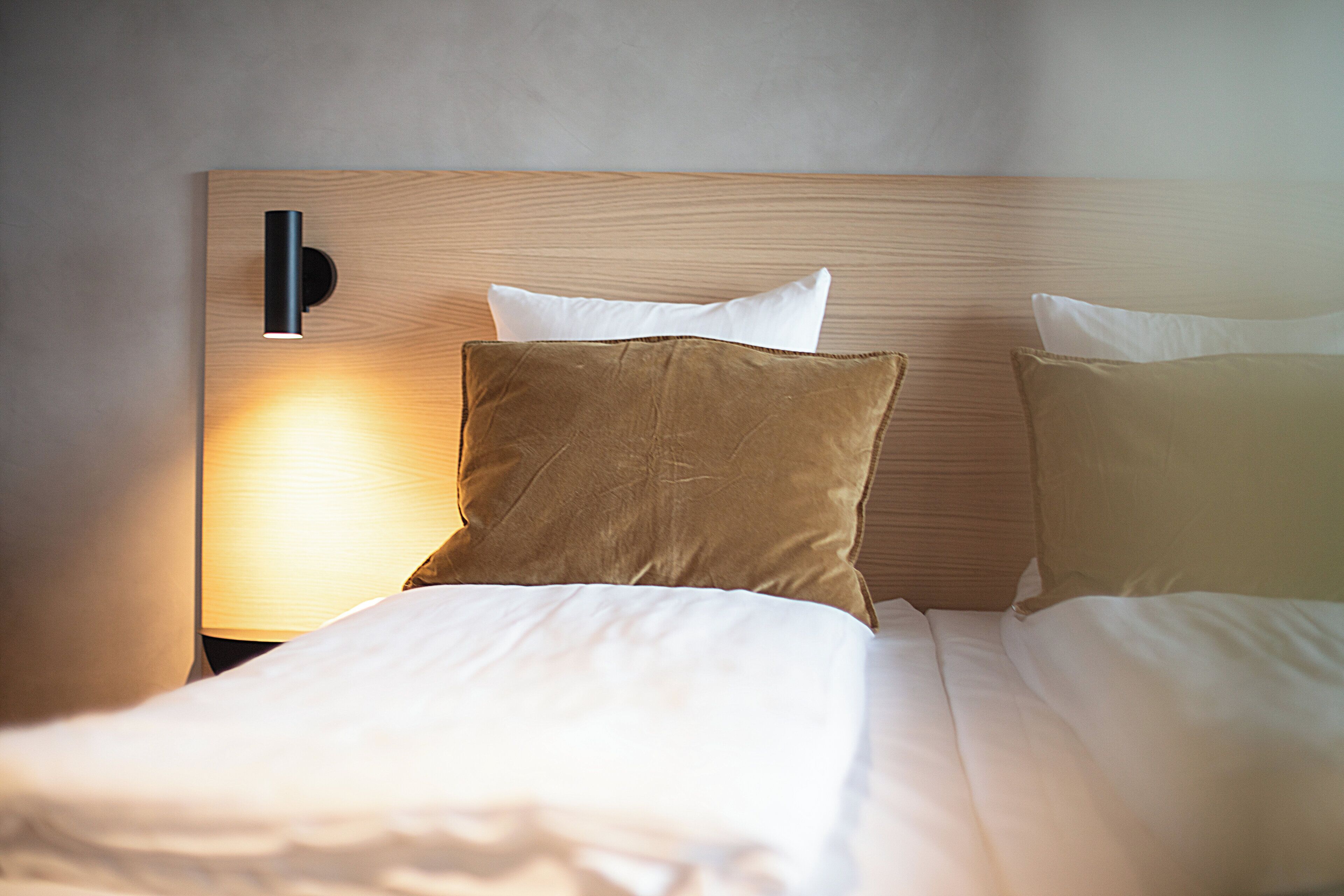 A neatly made bed with two pillows and a headboard with a light fixture.