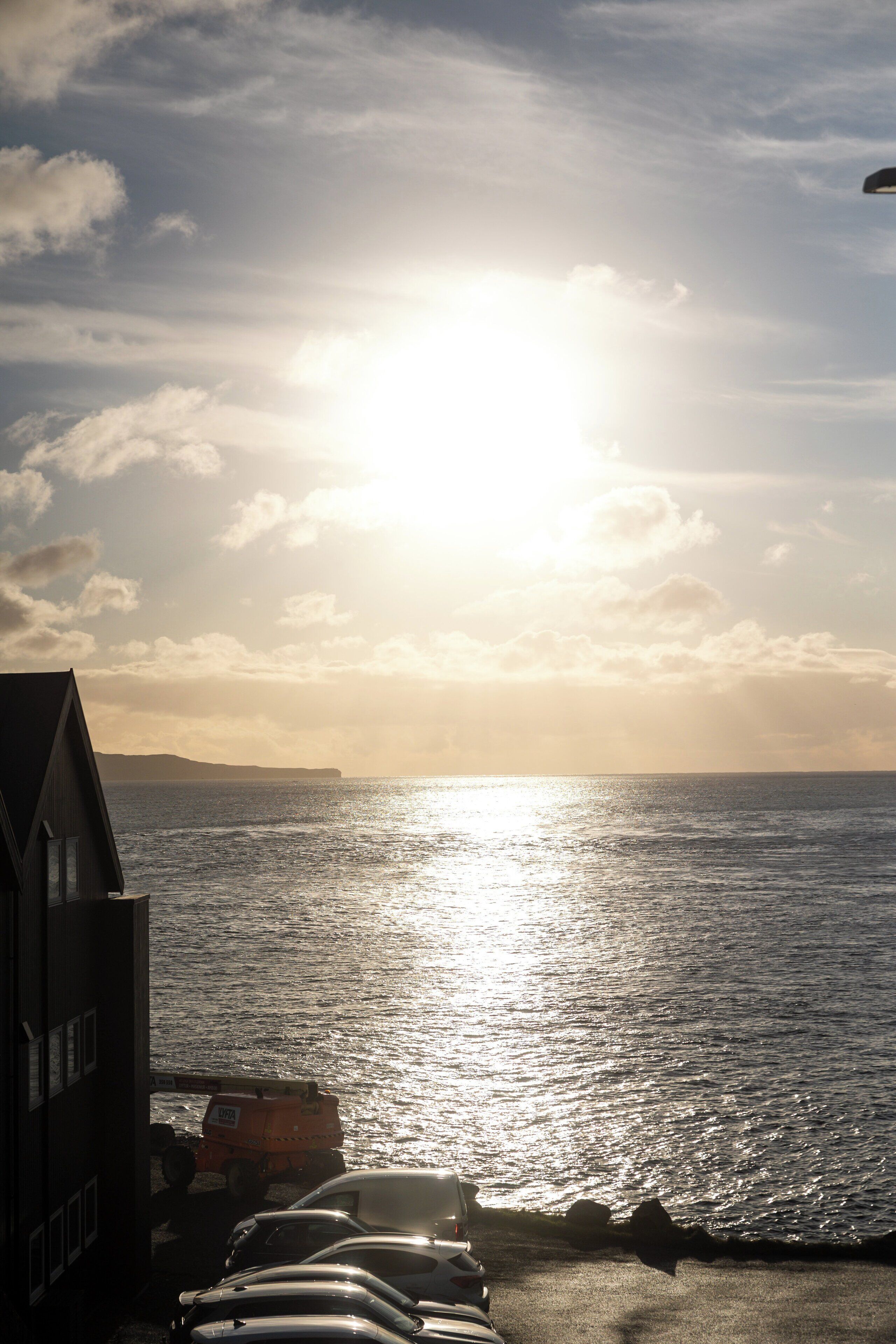 A sunset over the ocean with a building and parked vehicles in the foreground.