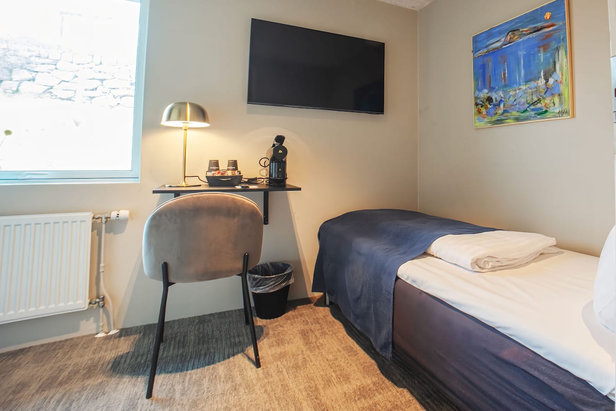 Une pièce comprenant un lit, une chaise, un bureau avec une lampe, un téléviseur et un tableau accroché au mur.