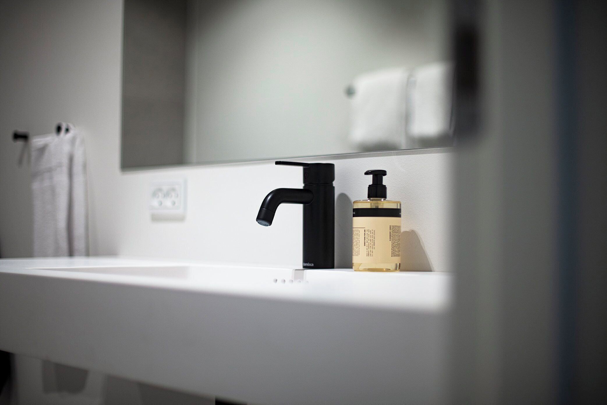 A bathroom with a white sink, a black faucet, and a bottle of hand soap.