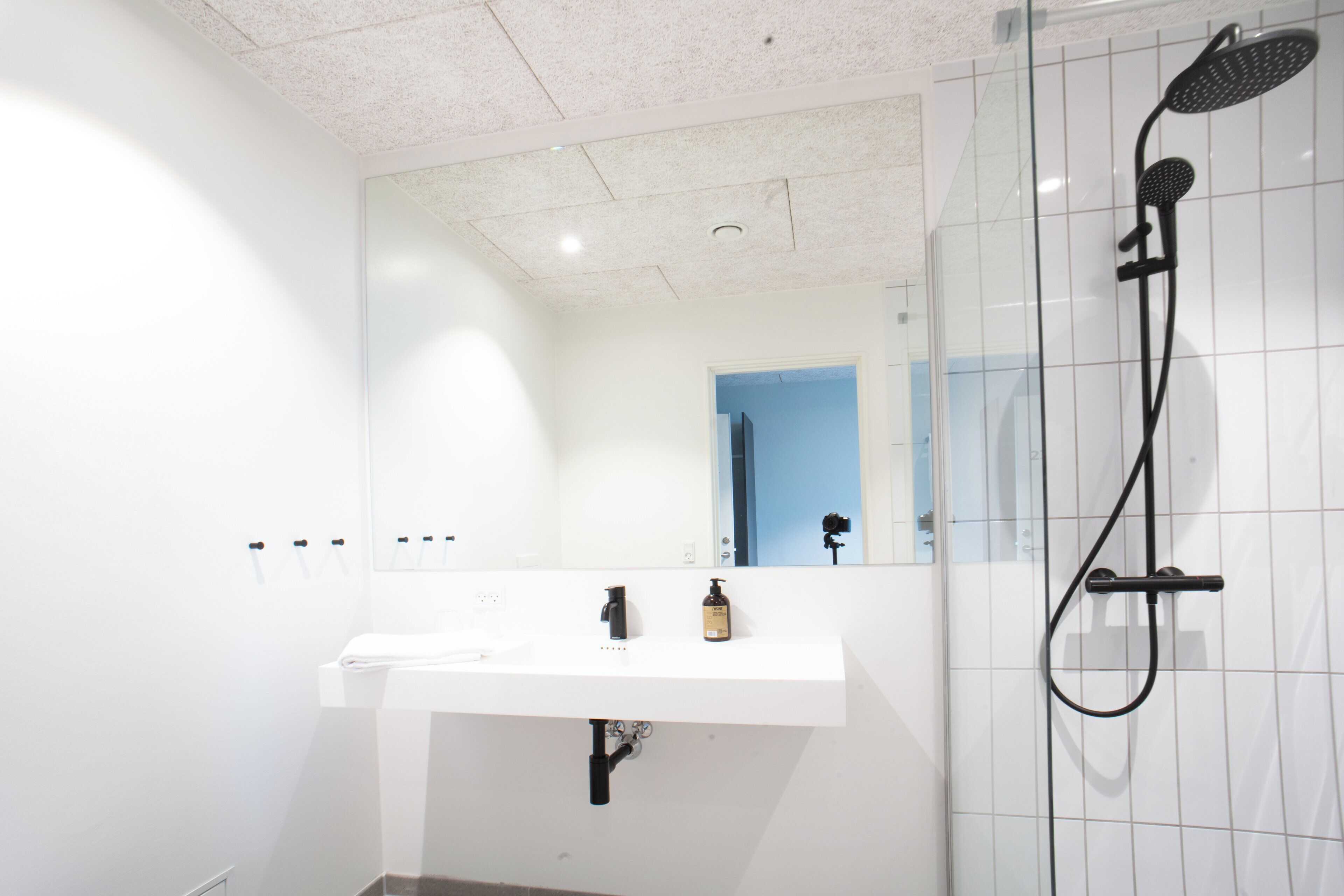 A modern bathroom with a white sink, a mirror, and a black showerhead.