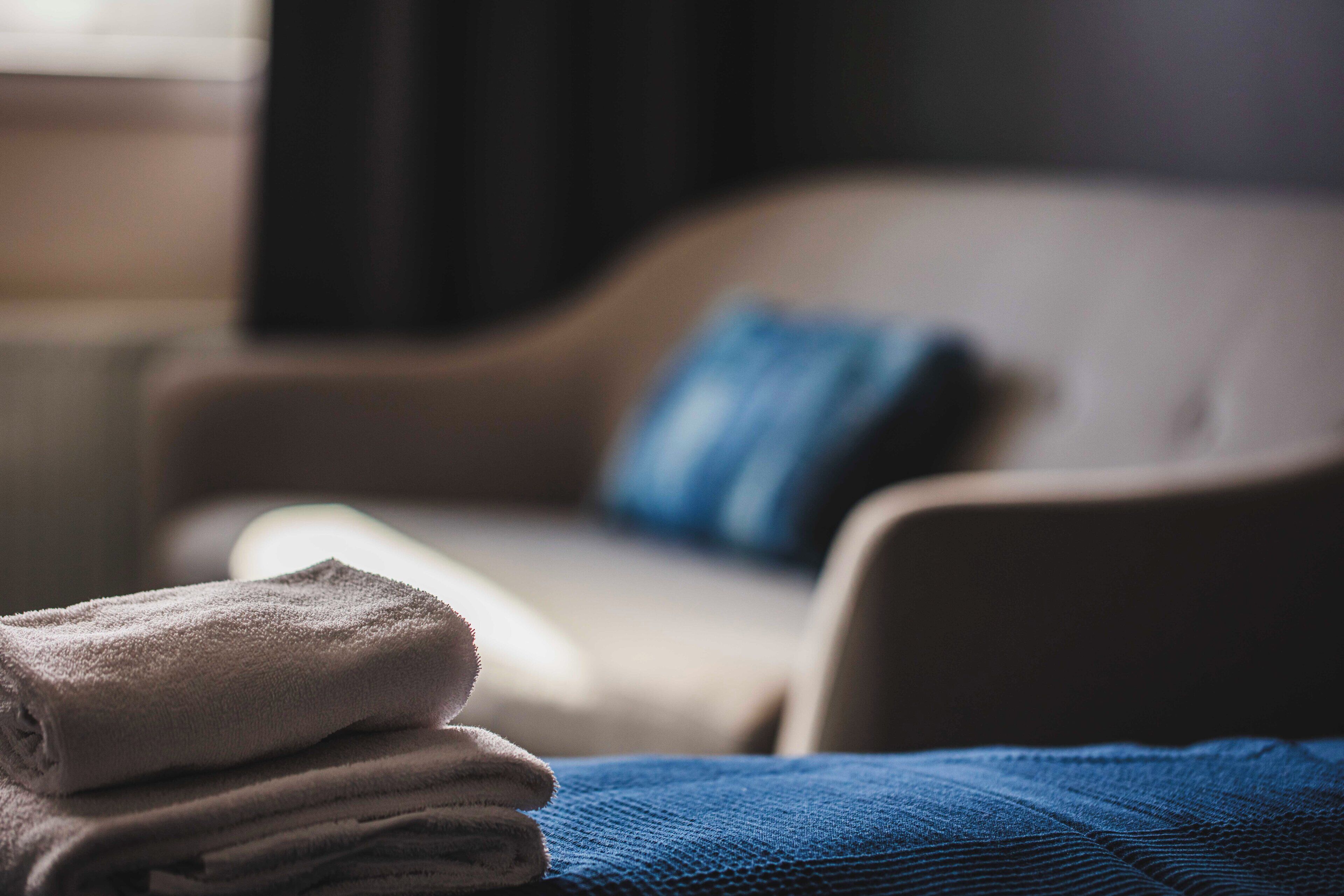 A stack of folded towels on a bed with a blue blanket.