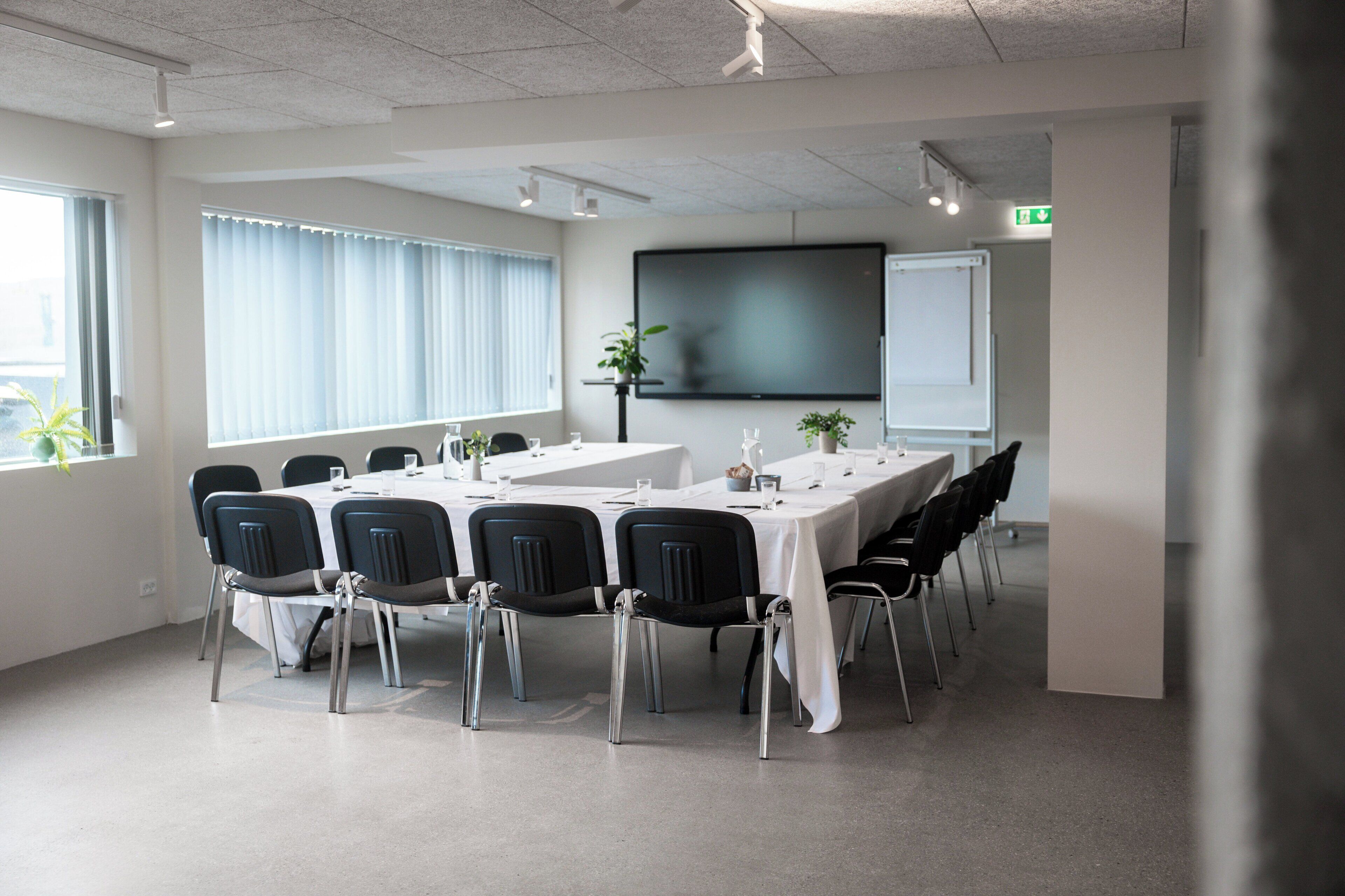 A conference room with a long table, chairs, a projector screen, and a whiteboard.