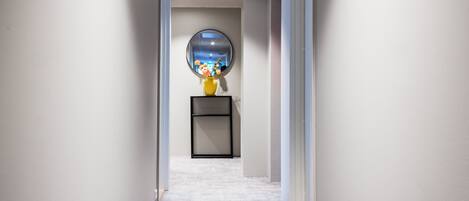 A hallway with a carpeted floor, a round mirror on a pedestal, and a framed picture on the wall.