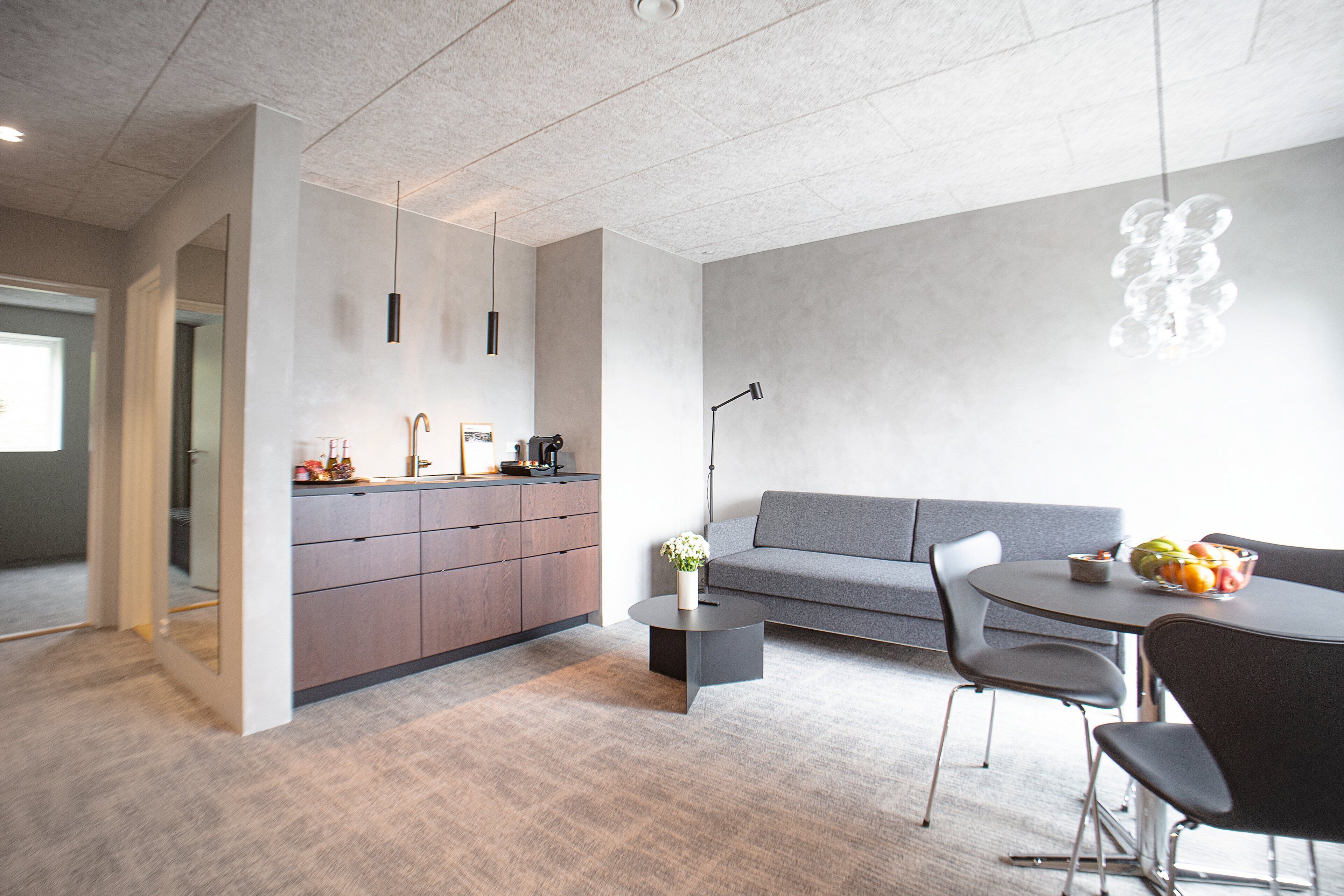 A modern kitchen with a grey sofa and dining area, featuring a round table with chairs and a small side table with a vase.