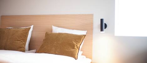 A neatly made bed with two pillows, a wooden headboard, and a wall-mounted light fixture.
