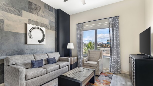 A modern living room with a grey sofa, a coffee table, a TV, and a view of the city through large windows. - Bluegreen Vacations Club 36, an Ascend Collection Resort (Las Vegas)