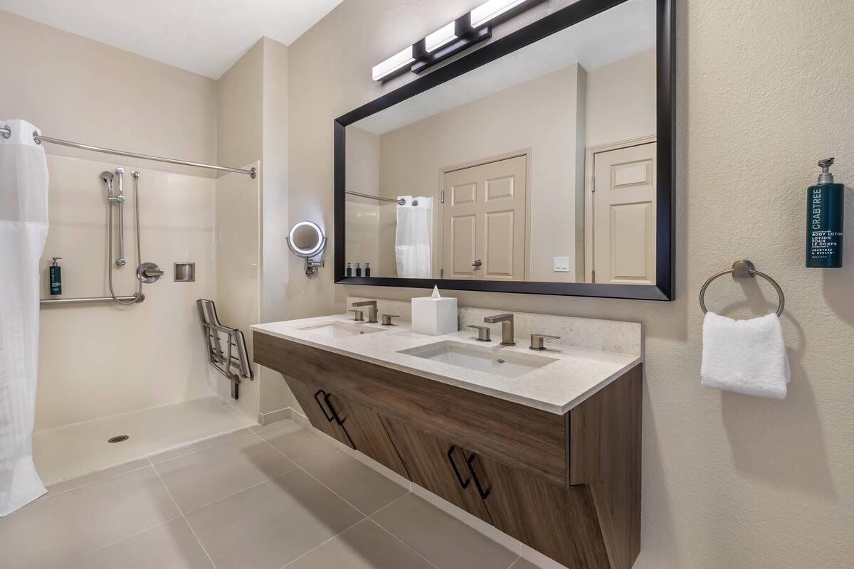 Un baño moderno con un espejo grande, lavamanos dobles, ducha y toallero.