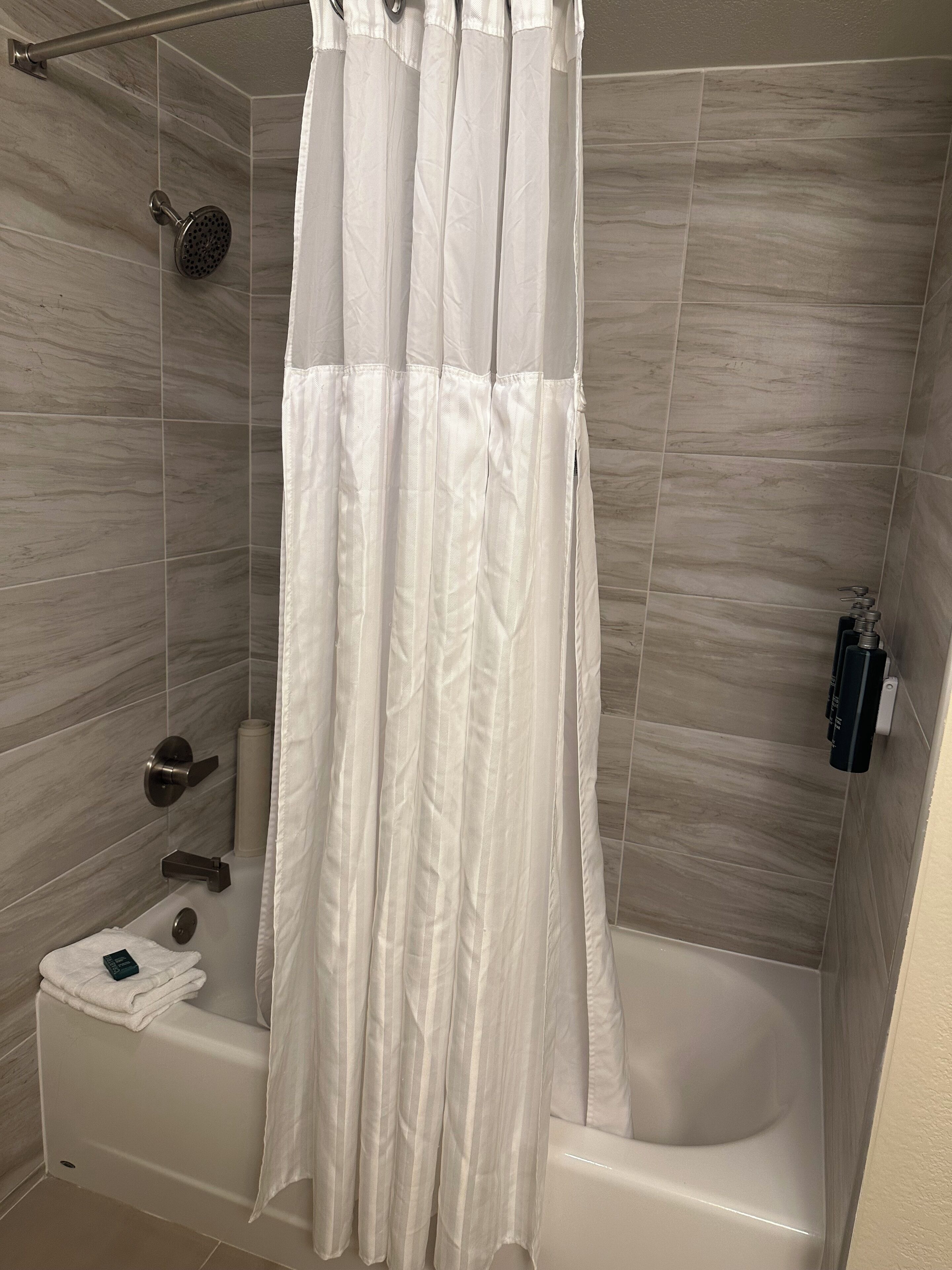 Une salle de bain avec un rideau de douche, un pommeau de douche amovible, une serviette et une bouteille de shampoing.