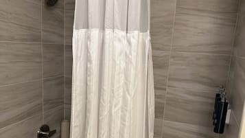 Une salle de bain avec un rideau de douche, un pommeau de douche amovible, une serviette et une bouteille de shampoing.