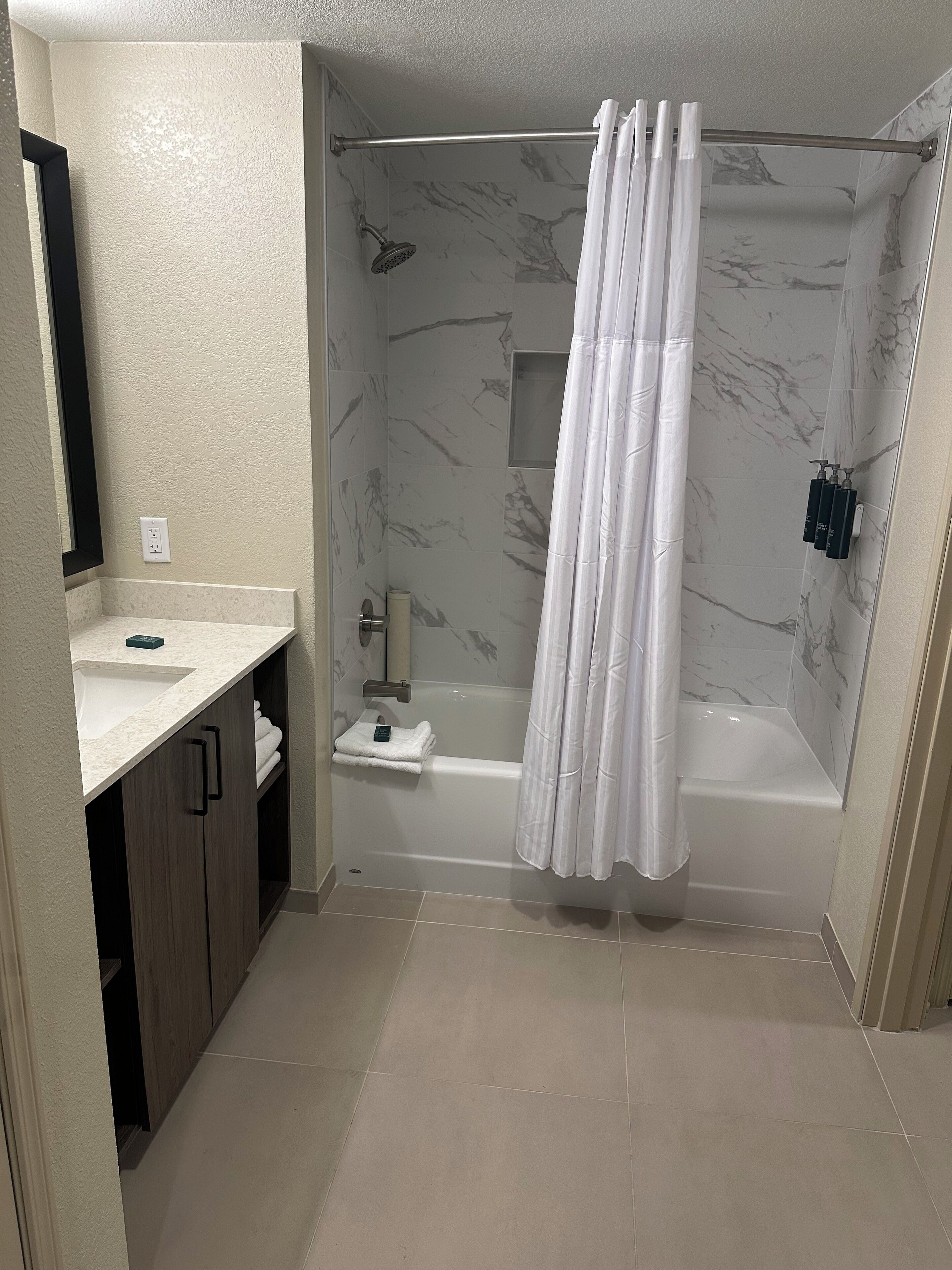 Un baño moderno con pared de ducha de mármol, bañera y tocador con lavamanos y espejo.