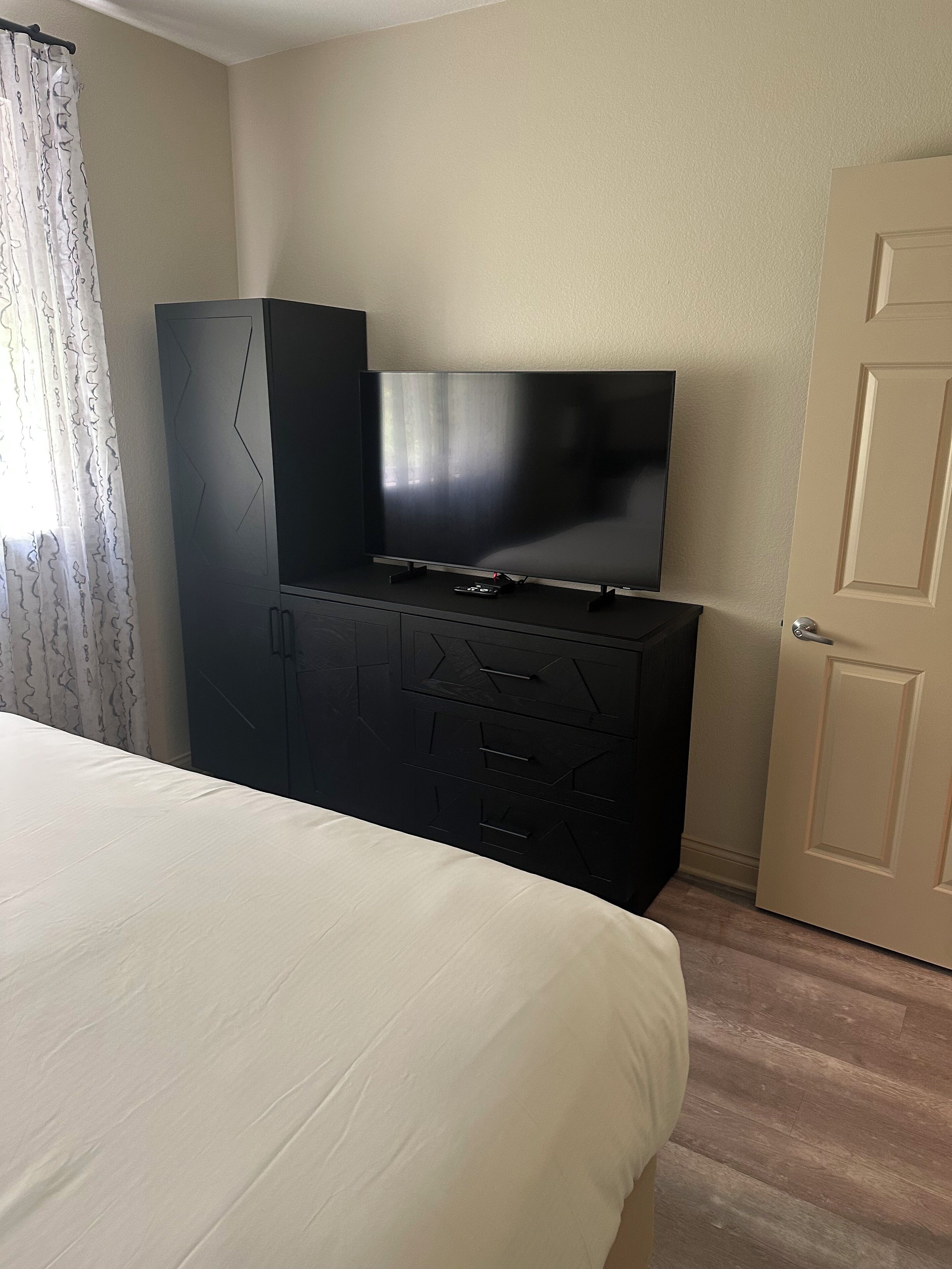 Une chambre d’hôtel avec un lit, un téléviseur posé sur un meuble noir et une porte.