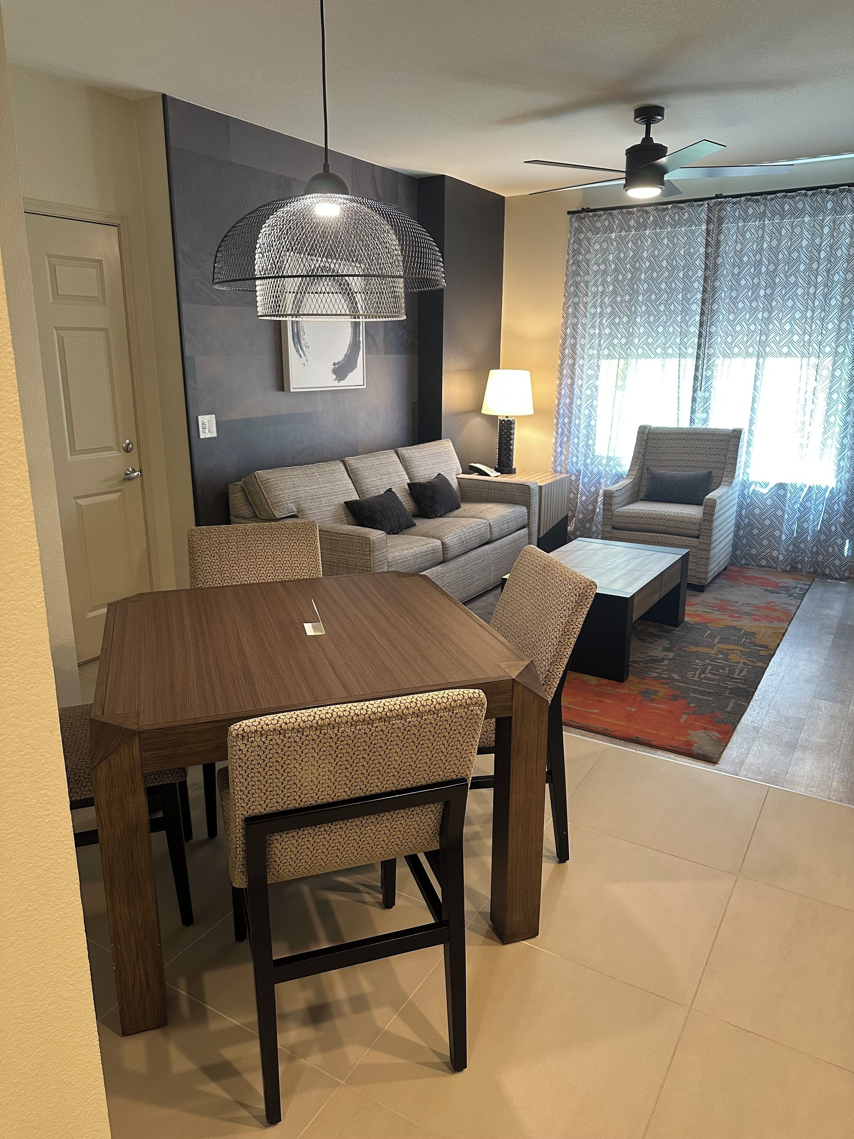 A modern living room with a dining area, a sofa set, a patterned rug, and a ceiling fan.