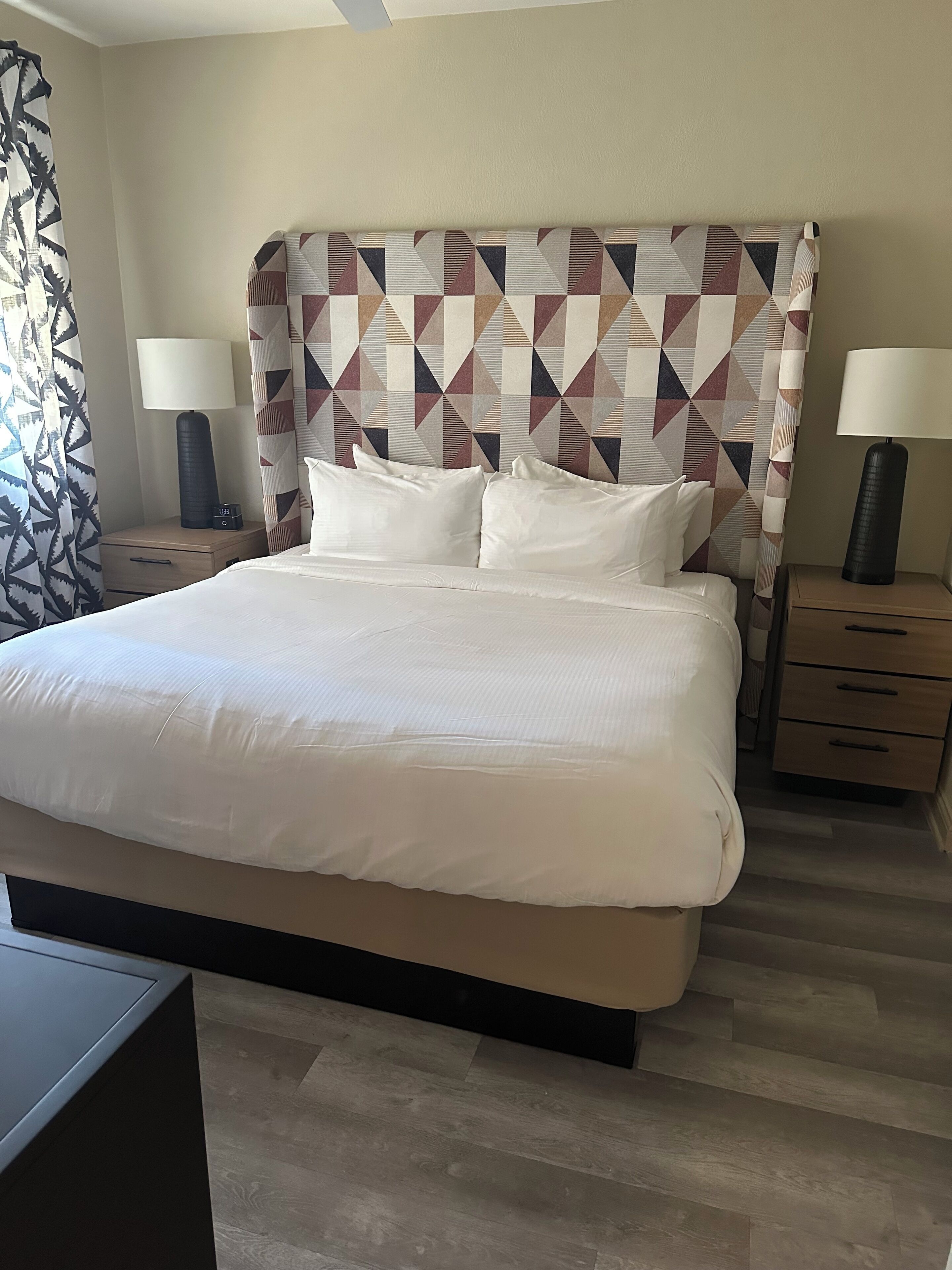 A neatly made bed with a patterned headboard, two bedside tables with lamps, and a wooden floor.