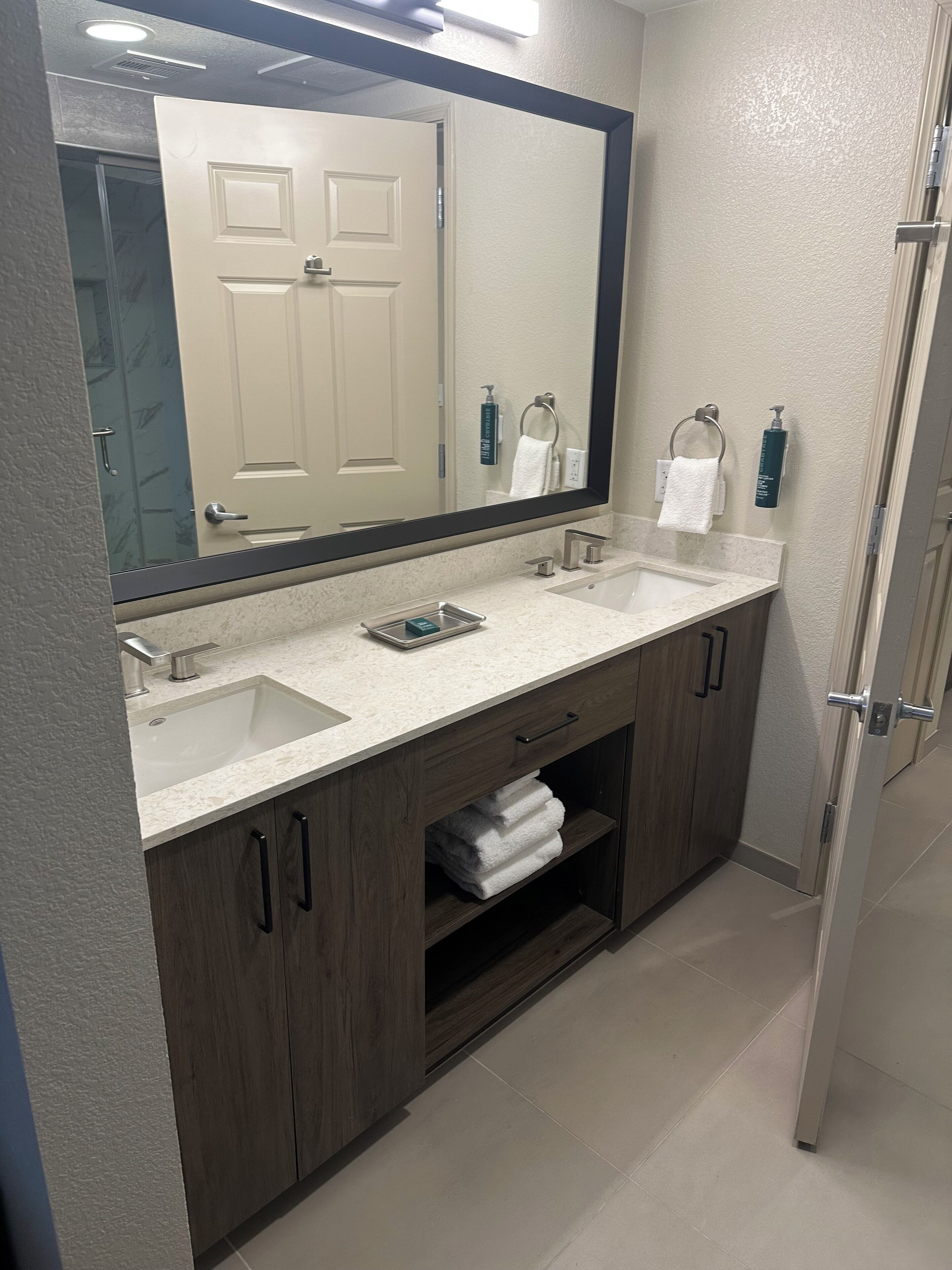A modern bathroom with two sinks, a large mirror, and a towel rack.
