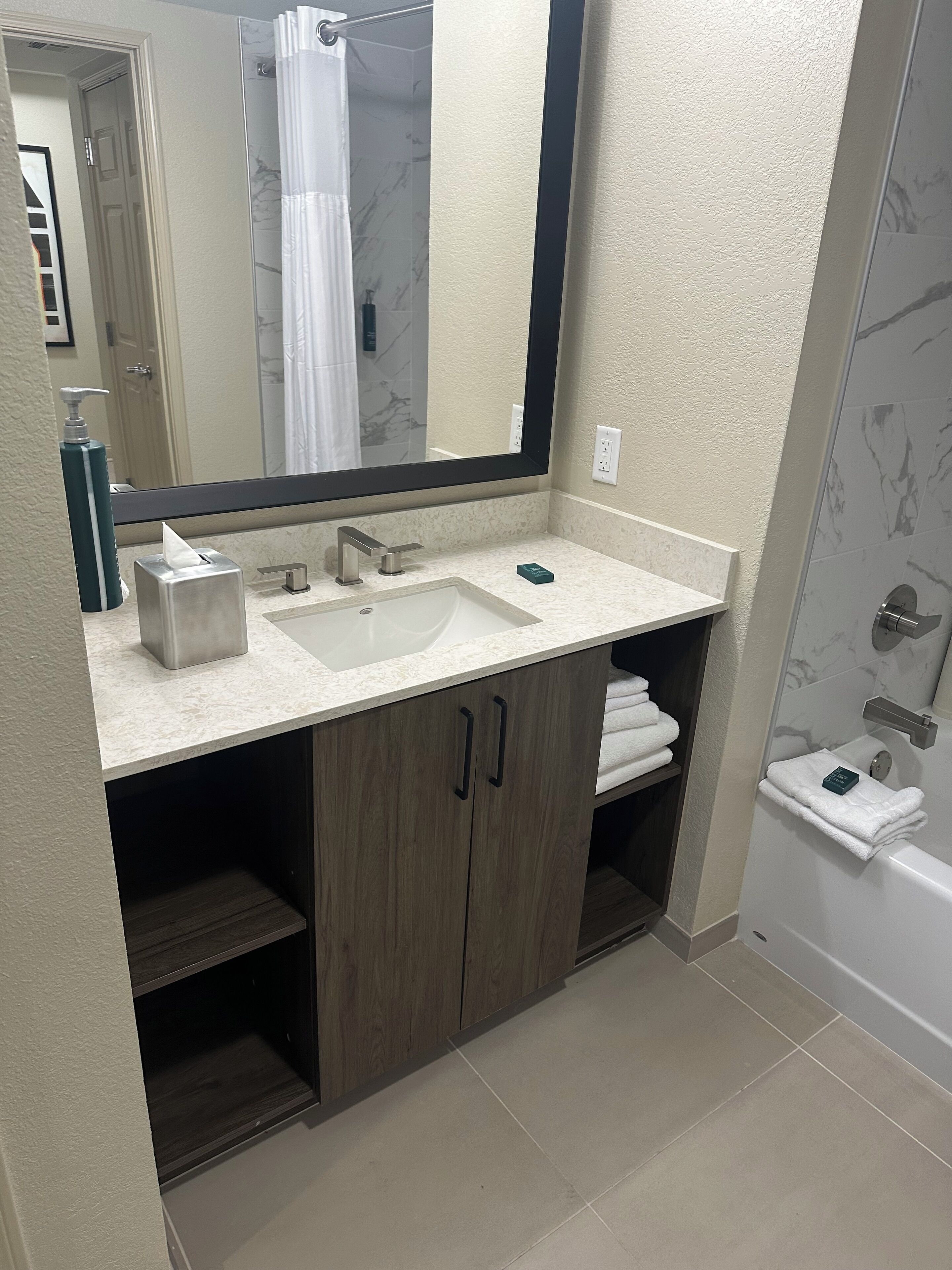 Un baño con lavamanos de mármol, armarios de madera, un espejo grande y una zona de ducha.
