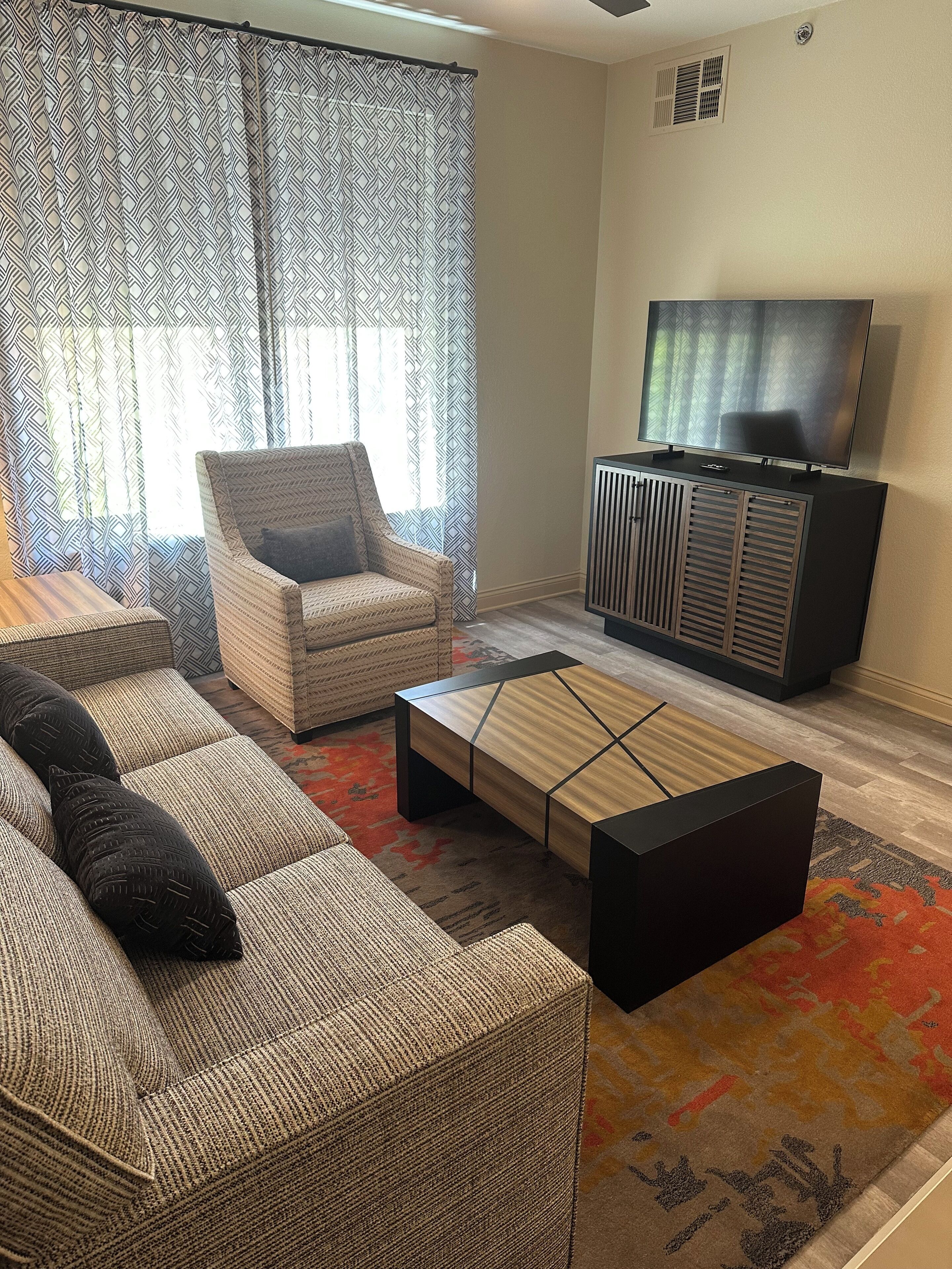 Una sala de estar con sofá, una mesa de centro, un televisor sobre un mueble y cortinas estampadas.