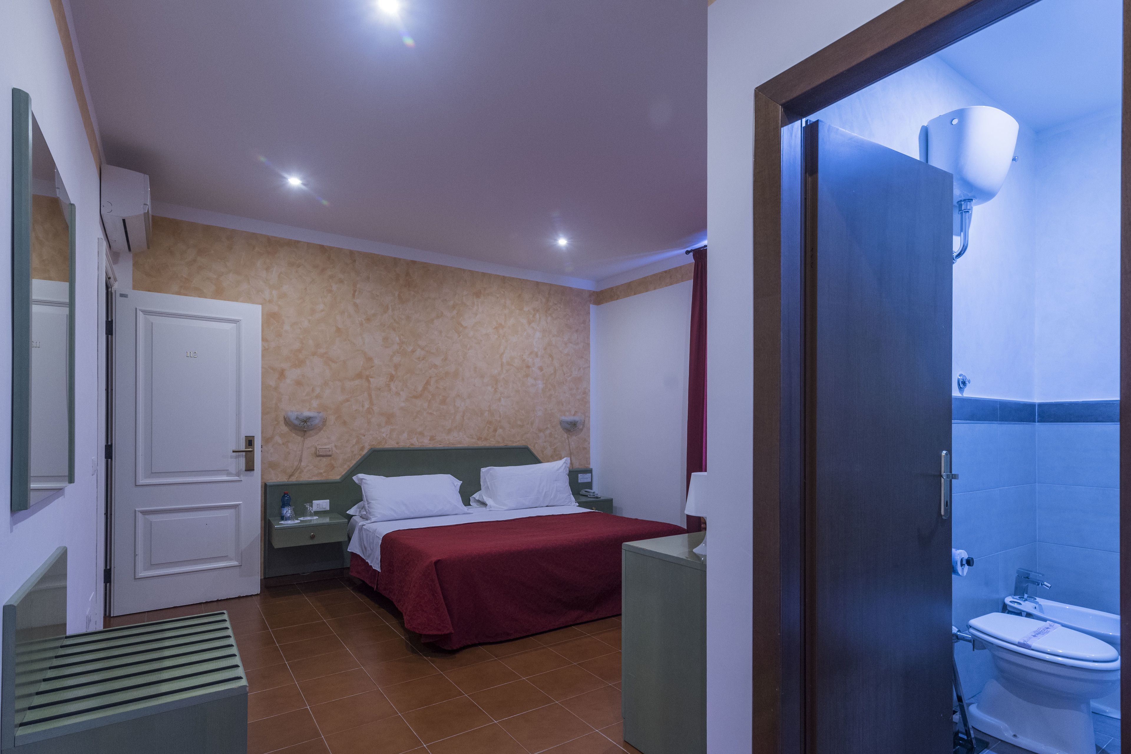 A hotel room with a bed, bedside table, and a bathroom with a toilet and sink.