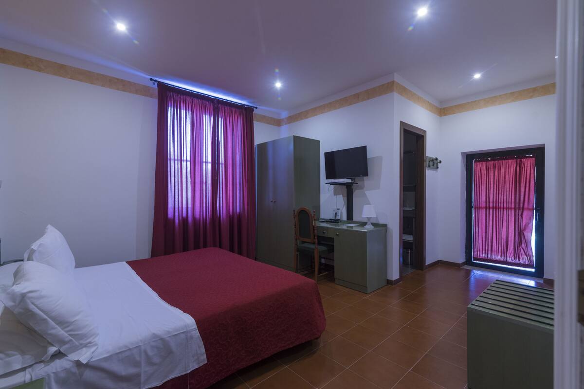 Habitació d'hotel amb llit, escriptori, cadira, televisió i finestra amb cortines.