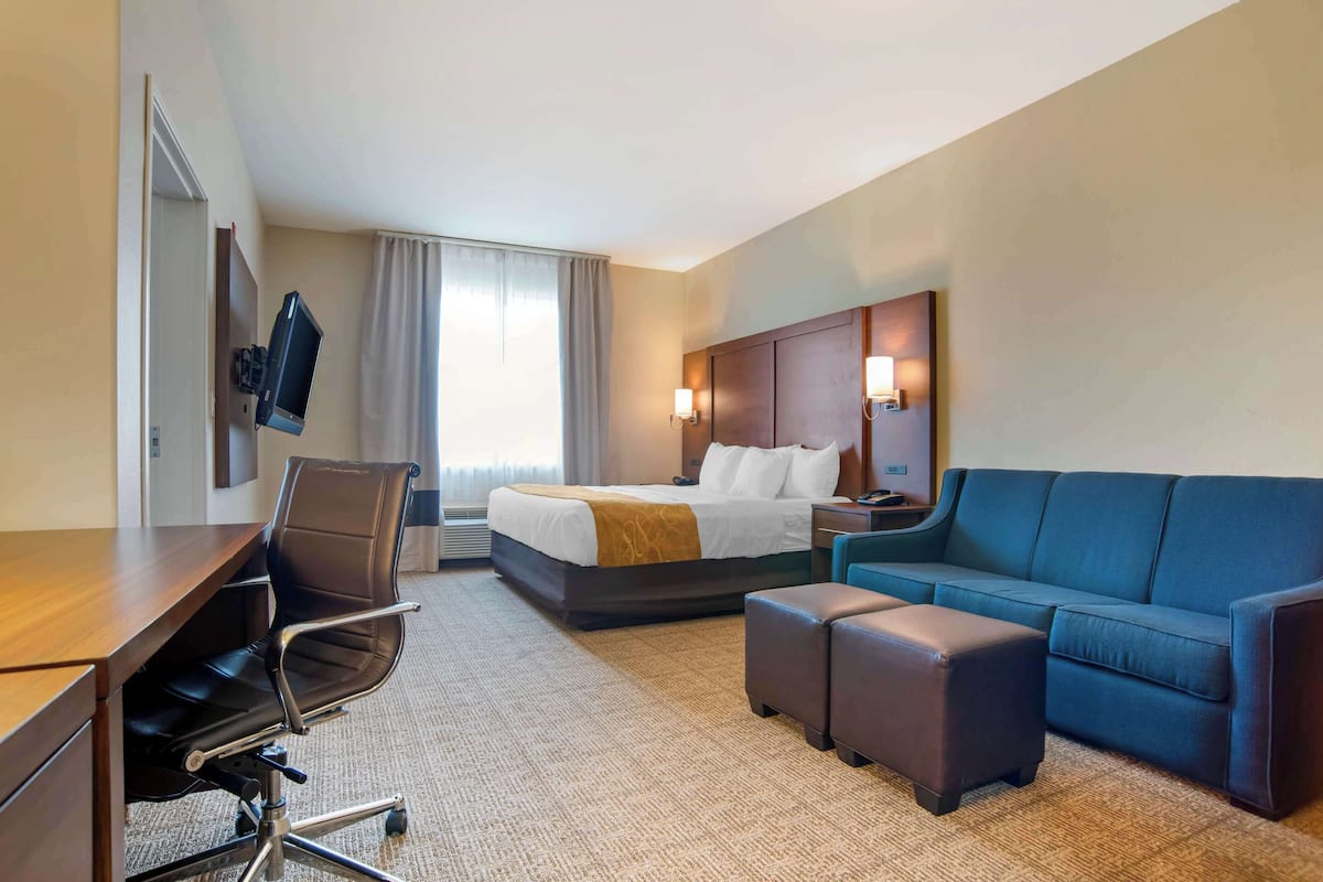 Une chambre d’hôtel équipée d’un lit, d’un bureau, d’une chaise, d’un canapé et d’un téléviseur fixé au mur.