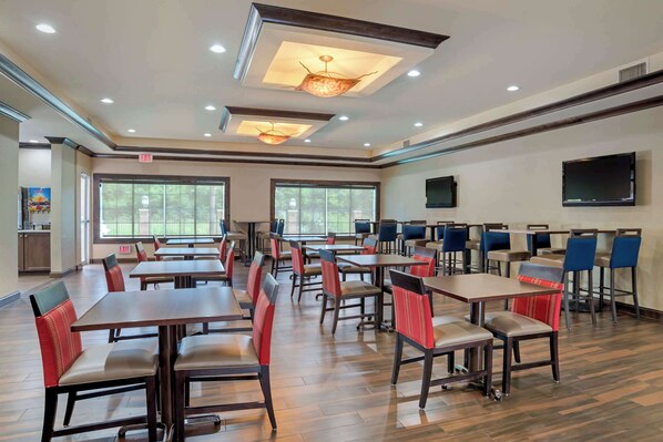 A spacious dining area with multiple tables and chairs, large windows, and a flat-screen TV mounted on the wall. - Comfort Suites Alexandria North (Alexandria)