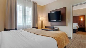 A hotel room with a large bed, a flat-screen TV mounted on the wall, a bedside table, and a lamp. - Comfort Suites Alexandria North (Alexandria)